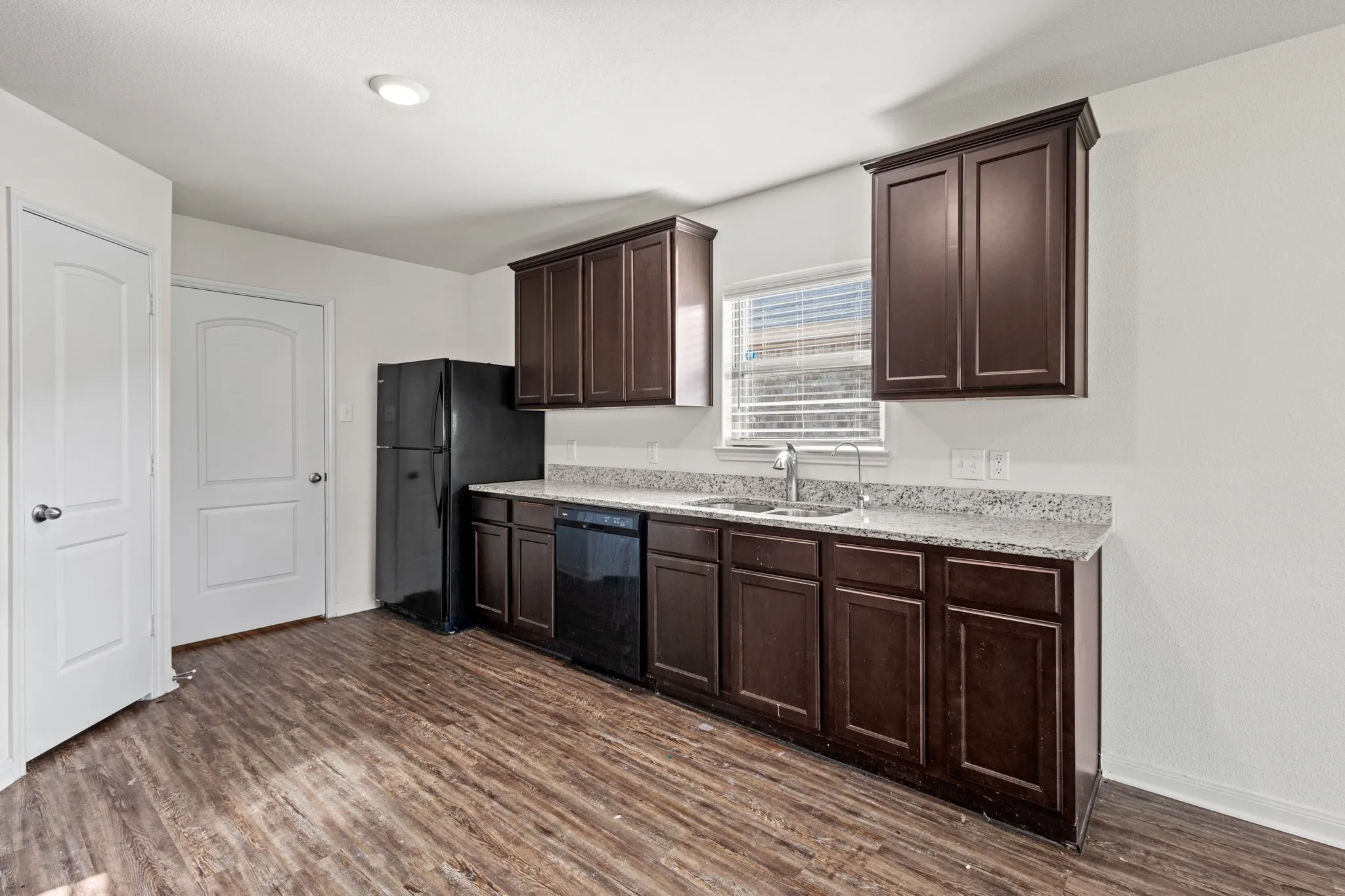 Kitchen featuring wood-finish flooring, dark wood cabinetry, light-toned granite countertops, and a stainless steel sink with a pull-down faucet