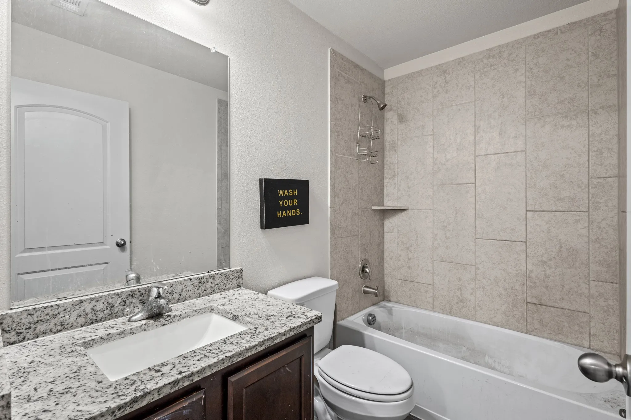 Bathroom featuring a built-in tub with tile surround, a dark wood-finish vanity with a light-toned countertop, an integrated sink, and a large wall-mounted mirror