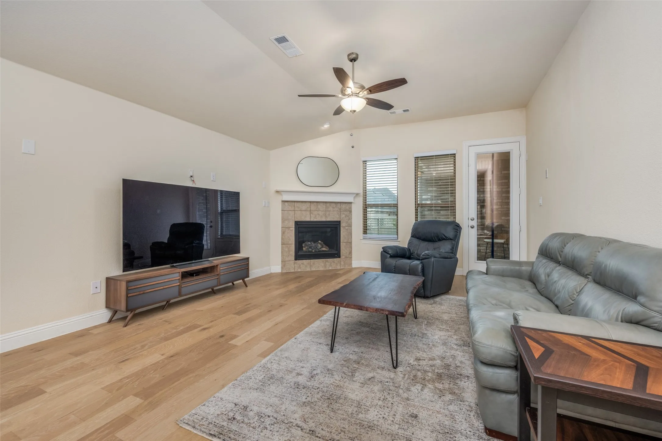 Bright living area featuring wood-finish flooring, a tile-surround fireplace, and a ceiling fan