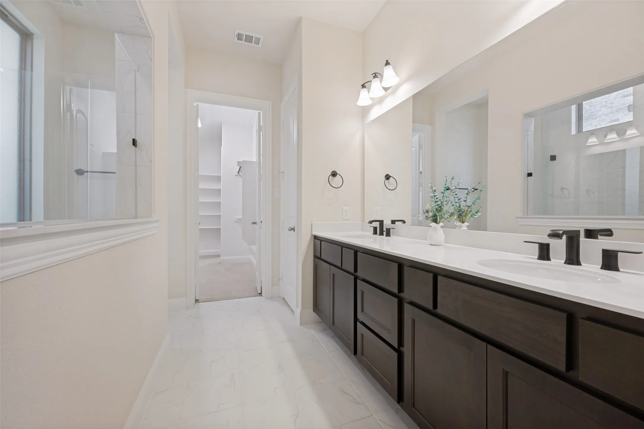 Spacious bathroom featuring a dual vanity with dark wood-finish cabinetry, white countertops, and matte black fixtures