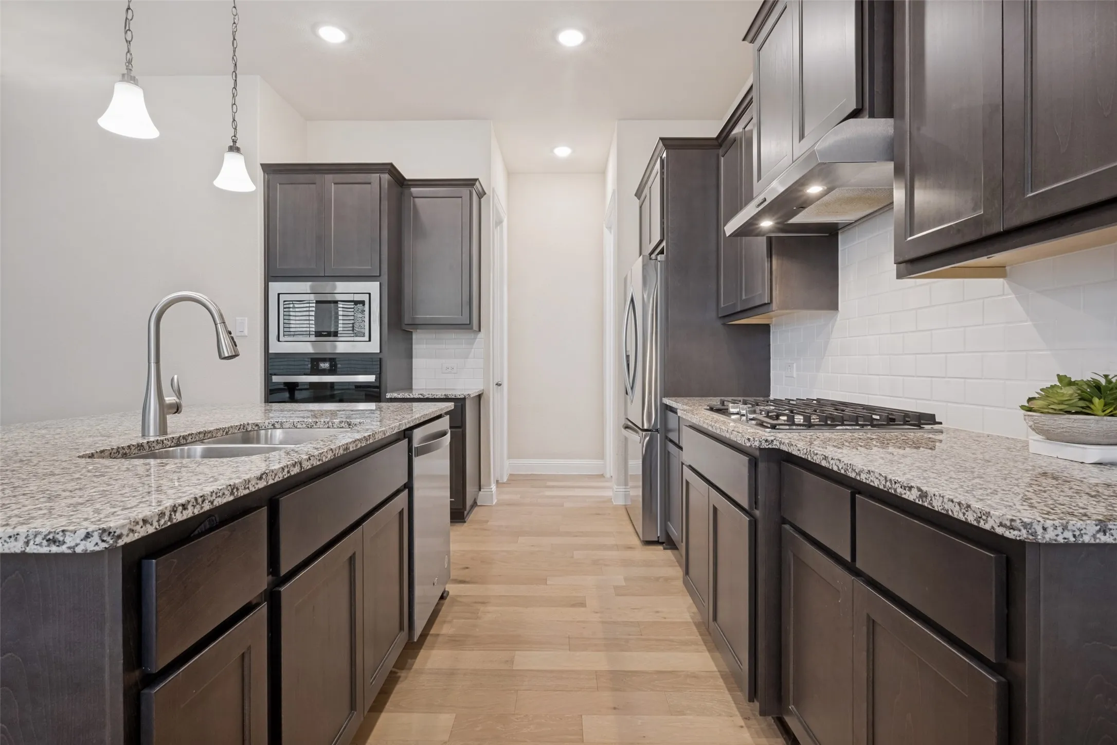 Kitchen featuring dark wood cabinetry, light granite countertops, stainless steel appliances, and light wood-finish flooring
