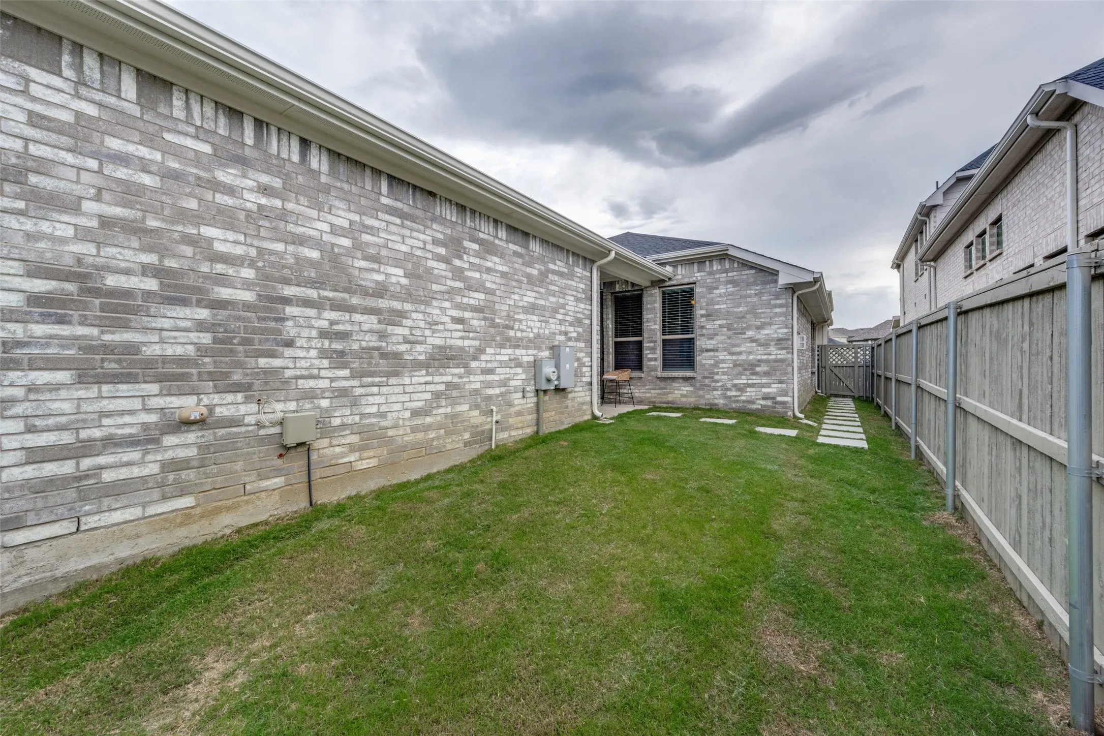 Side yard featuring a green lawn, grey brick exterior, and a wooden privacy fence
