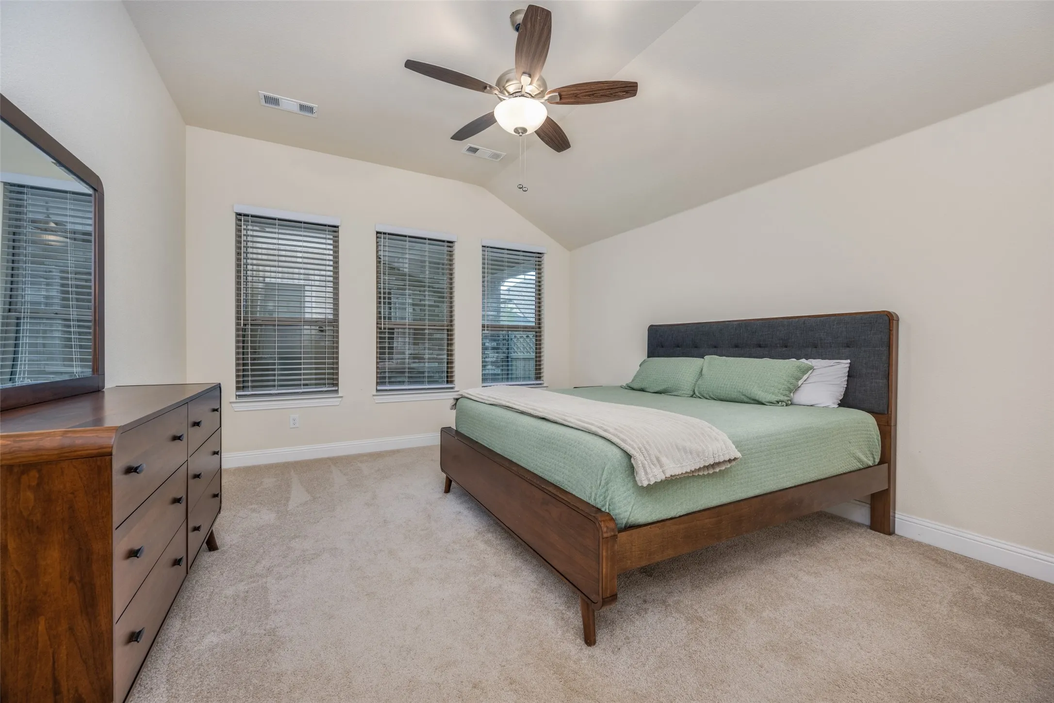 Vaulted ceiling bedroom with light beige carpeting and three large windows featuring horizontal blinds