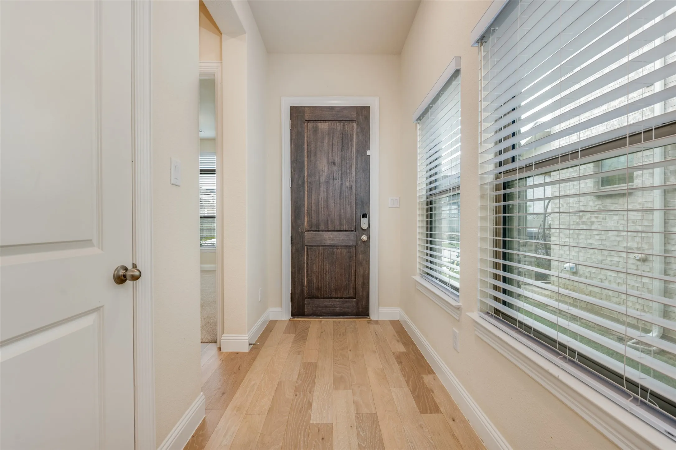 Entryway featuring wood-finish flooring, a dark wood-paneled door, and two windows with blinds