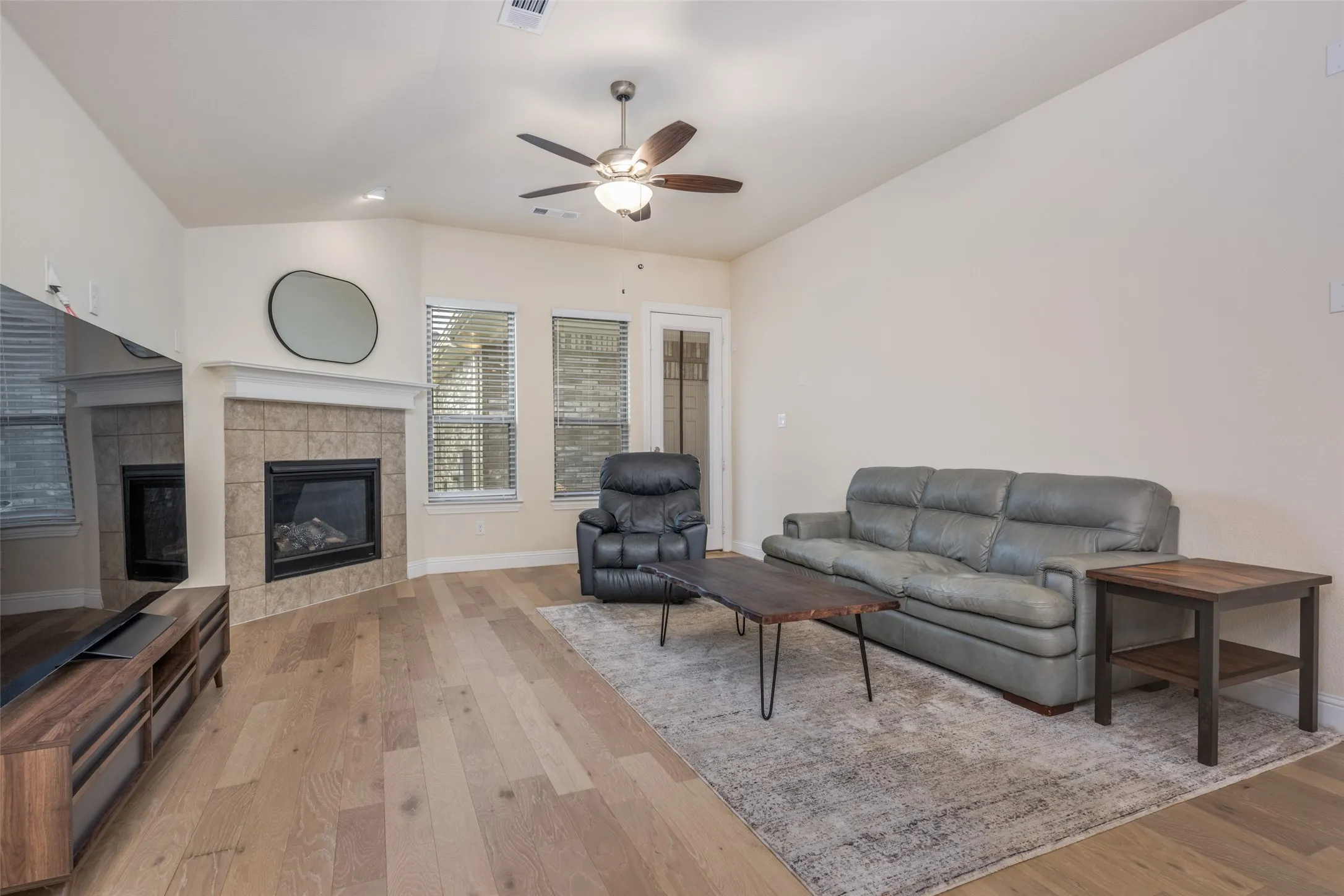 Living area featuring wood-finish flooring, a corner fireplace with a tiled surround and mantel, and vaulted ceilings