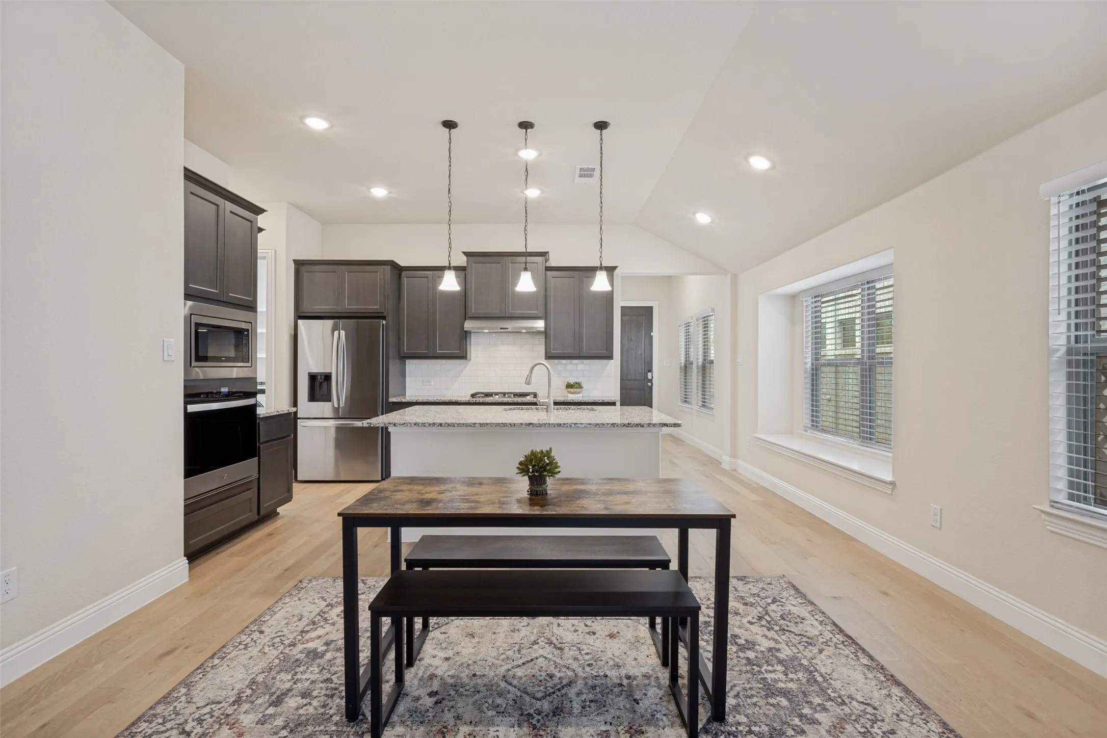 Open-concept kitchen featuring dark wood cabinetry, stainless steel appliances, a center island with a white countertop, and pendant lighting
