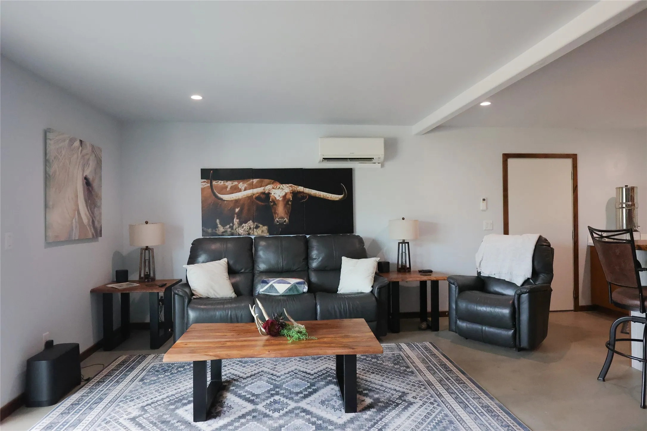Open concept living room with a quartz kitchen island, dining area and large picture windows. Sealed concrete floors and mini split climate control run throughout this Central Texas ranch home.