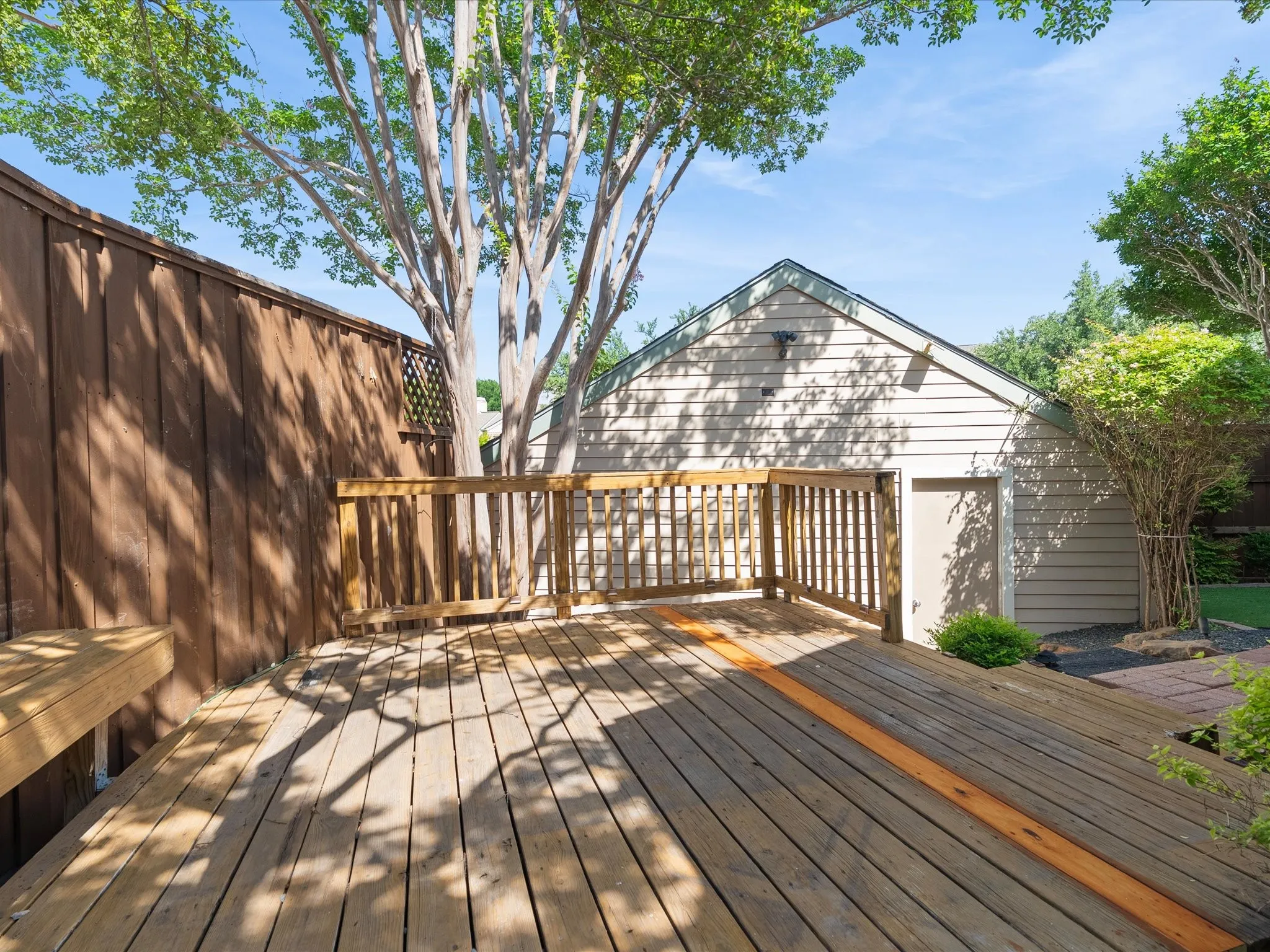 Wood deck with railing and integrated bench seating, featuring a privacy fence and mature trees