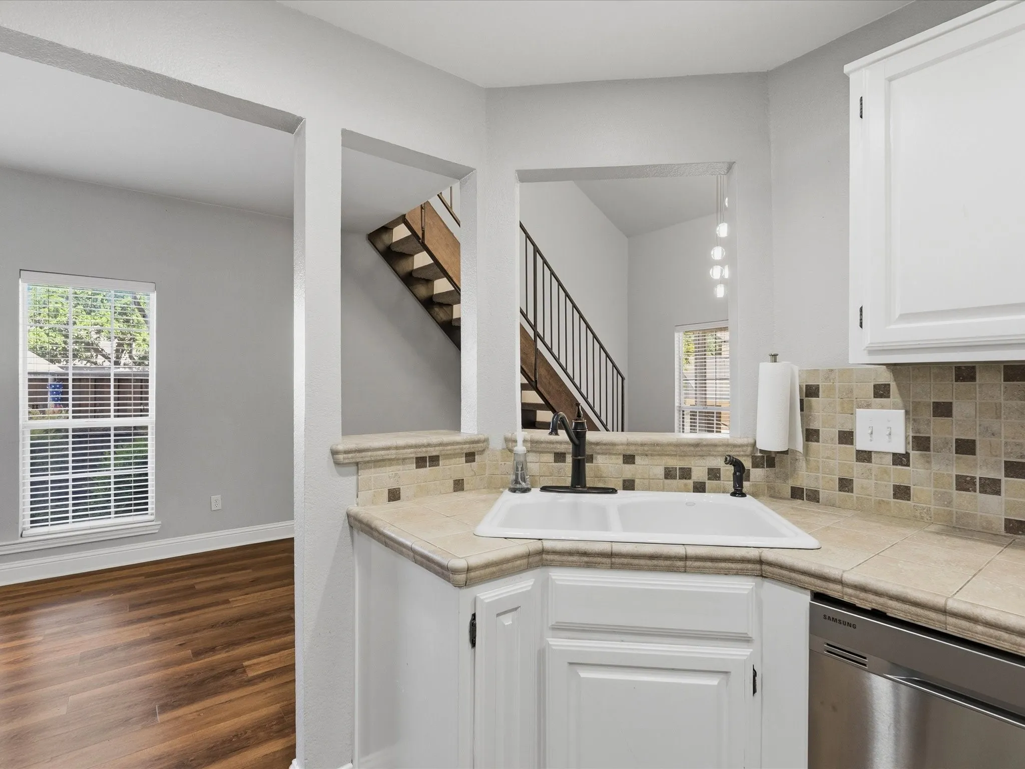 White kitchen cabinetry with a double basin sink, tile backsplash, stainless steel dishwasher, and wood-finish flooring