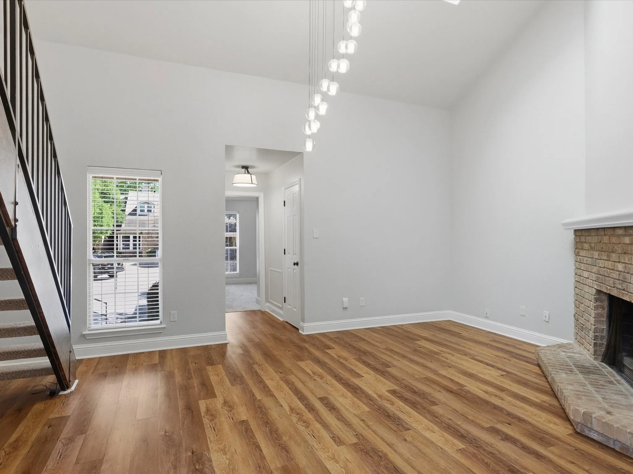 Vaulted ceiling with linear pendant lighting, wood-finish flooring, and a brick fireplace