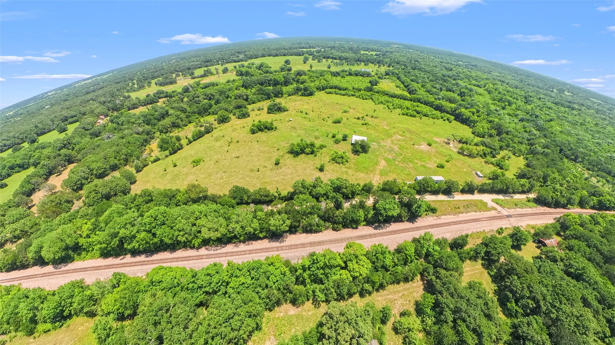 Expansive acreage featuring established tree lines, open pastures, and multiple outbuildings