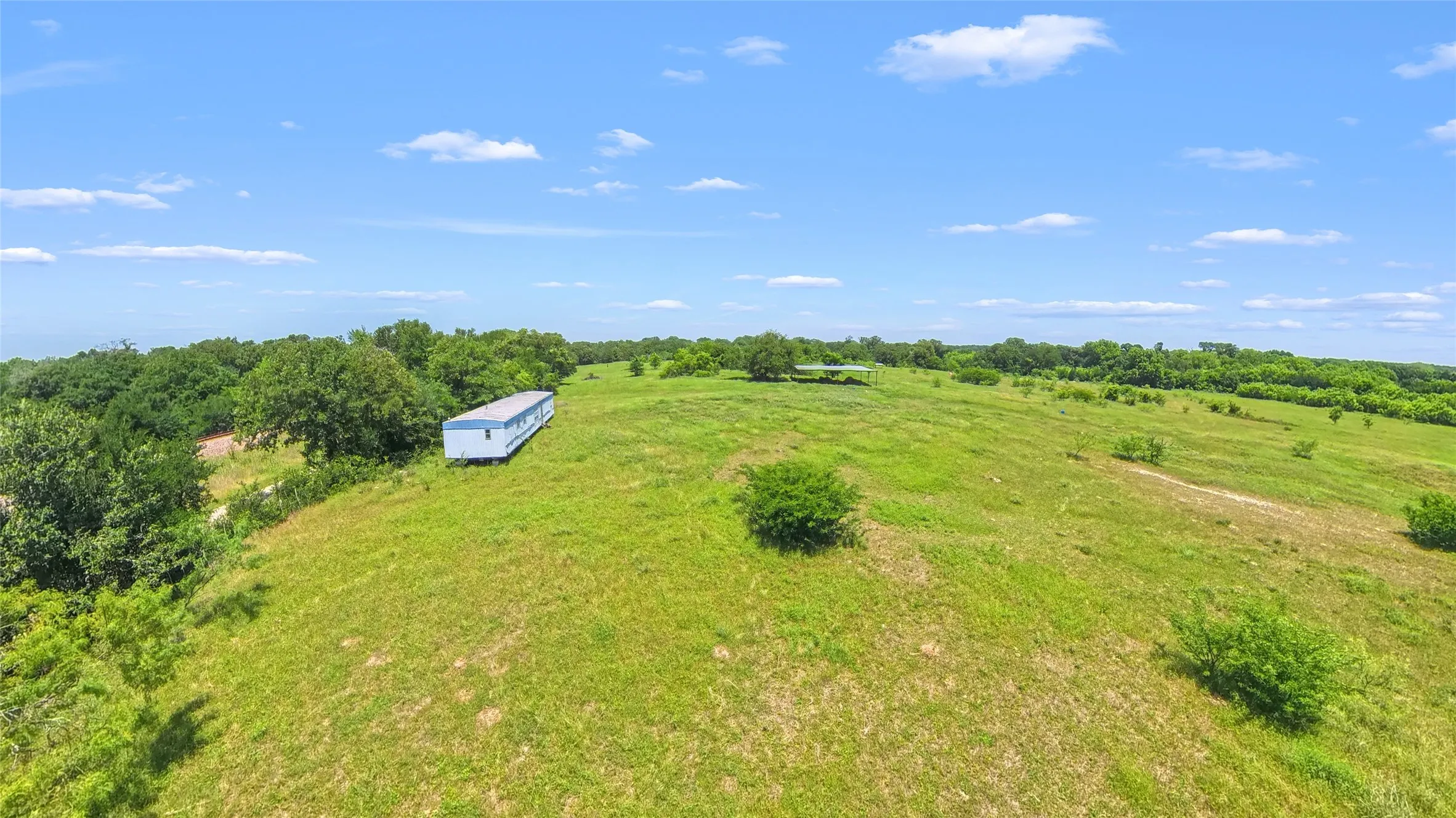 Expansive open land featuring diverse topography, scattered mature trees, and a distant structure