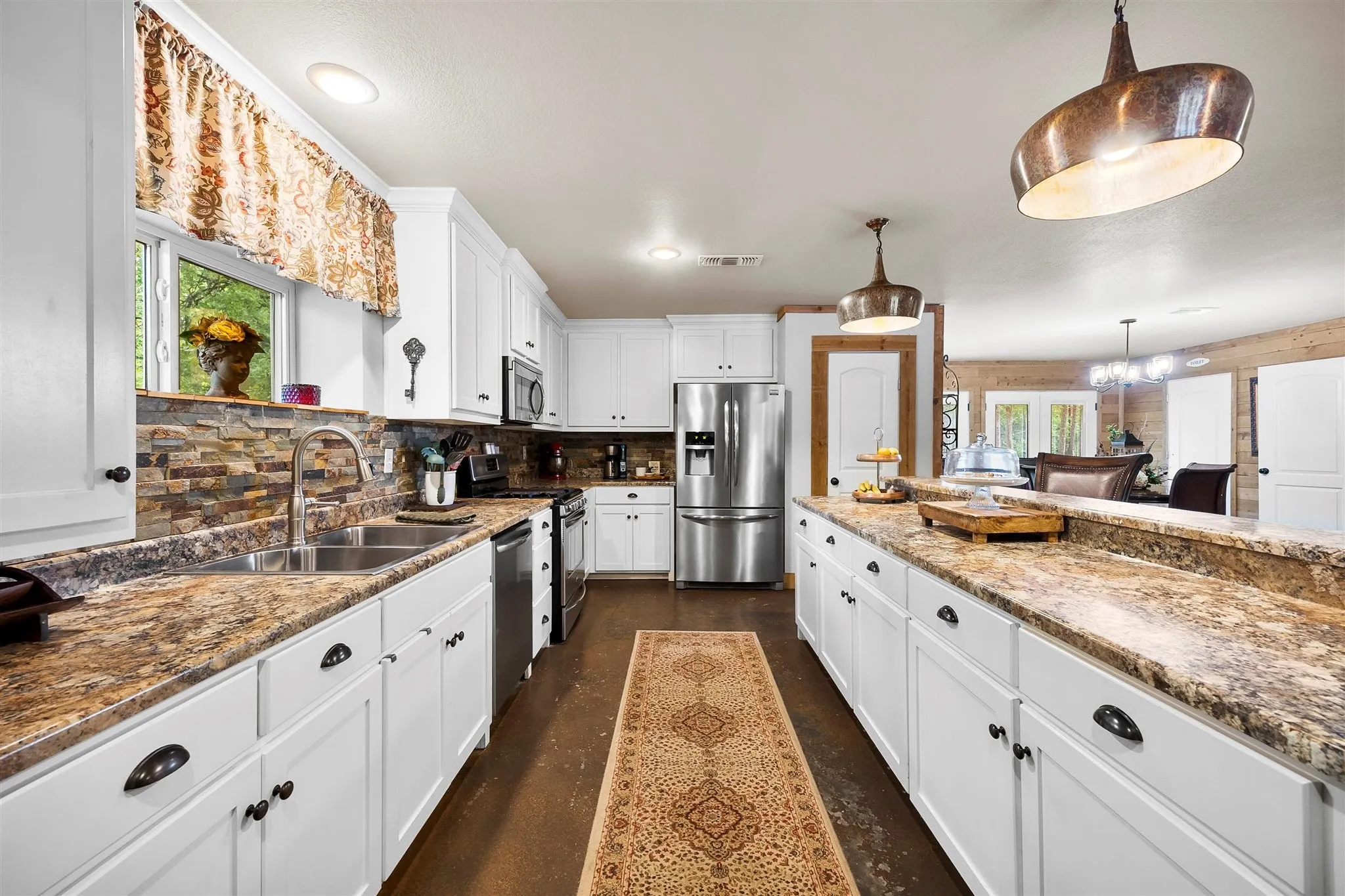 Kitchen featuring white cabinetry with dark hardware, stone-finish countertops, stainless steel appliances, and a stacked stone backsplash