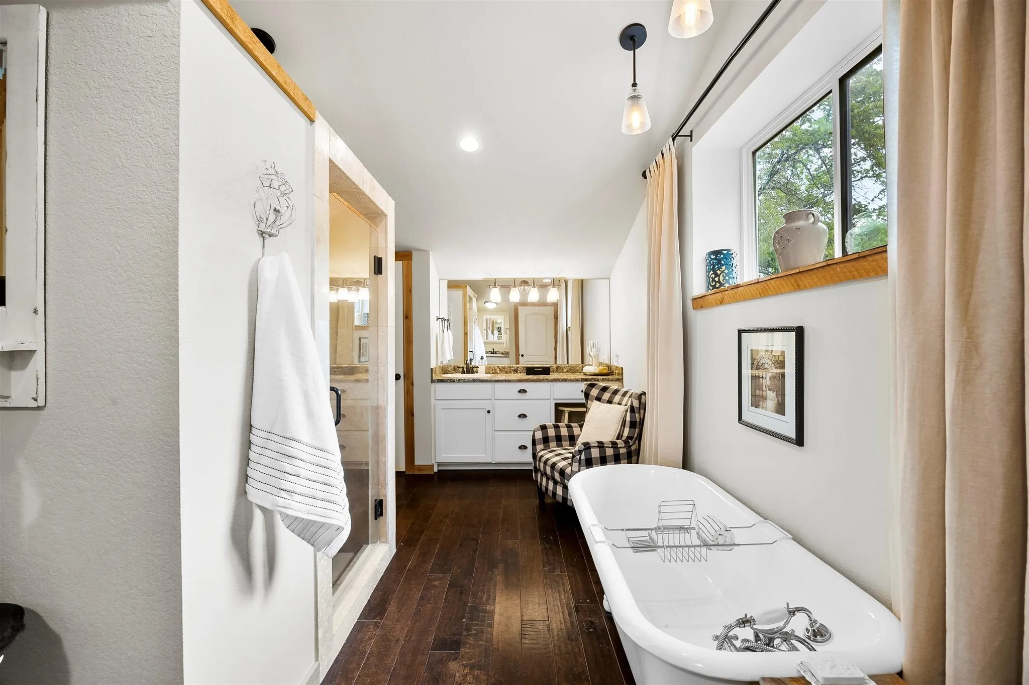 Freestanding soaking tub with dark wood-finish flooring, white walls, and a window with a wood sill