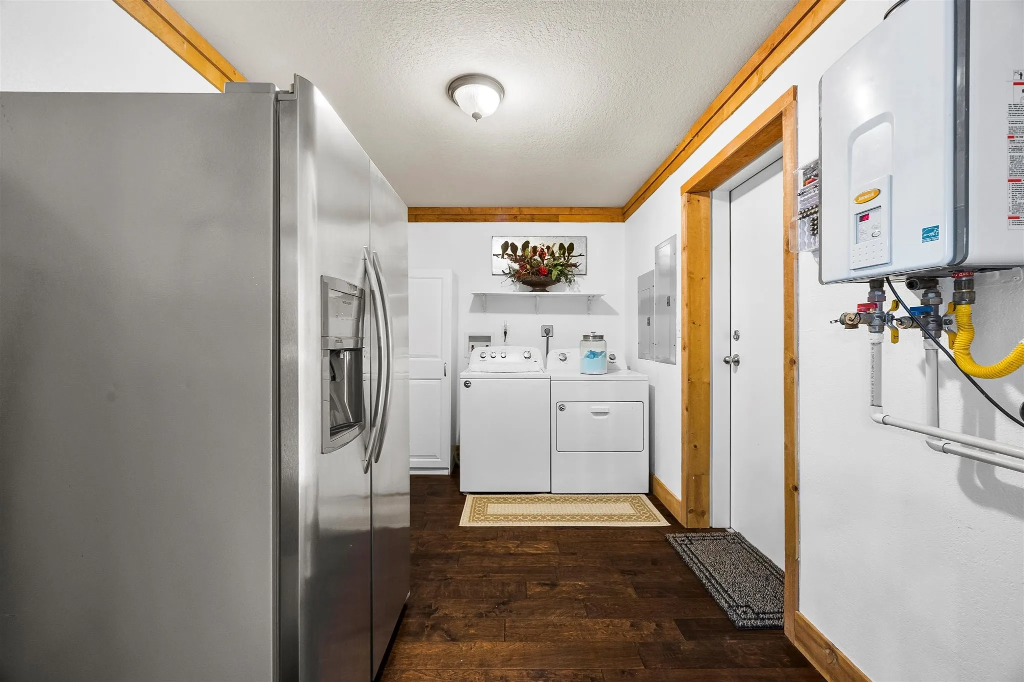 Utility area featuring wood-finish flooring, a stainless steel refrigerator, white walls, and wood trim accents