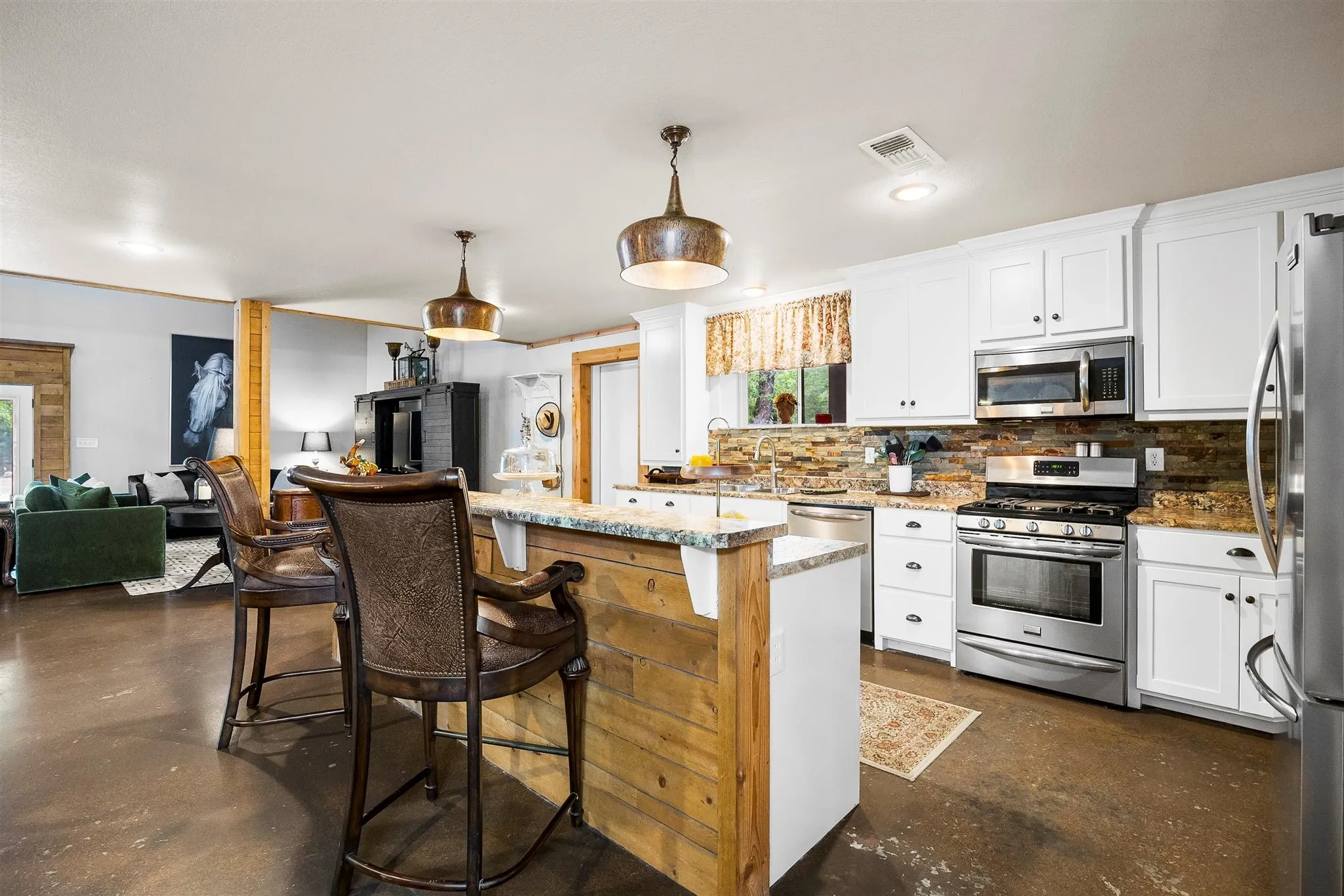 Kitchen featuring white cabinetry, stainless steel appliances, a stone tile backsplash, a center island with a wood-finish base, and pendant lighting