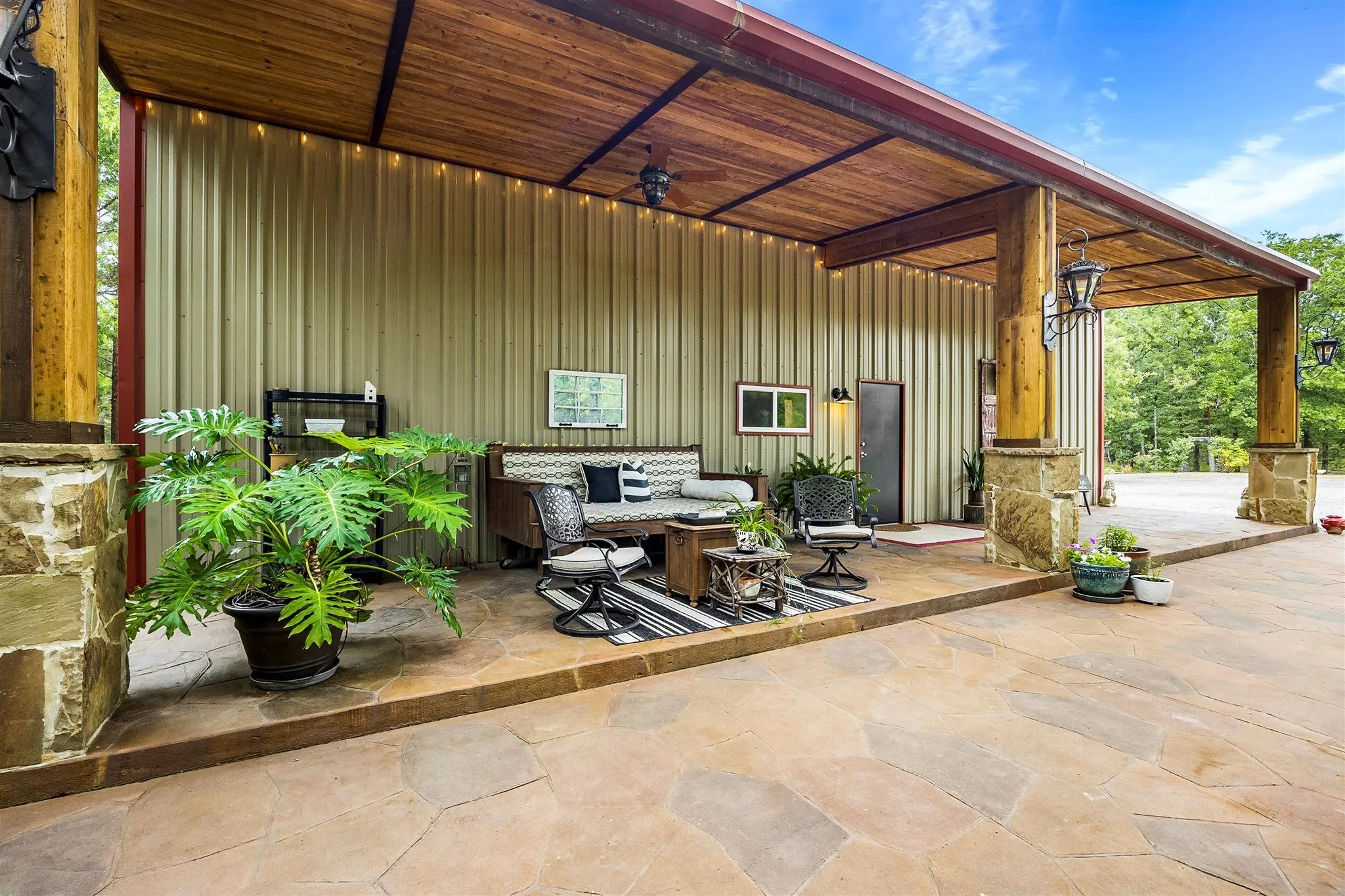 Expansive covered patio featuring a flagstone-style surface, a wood plank ceiling, and stone-clad support pillars