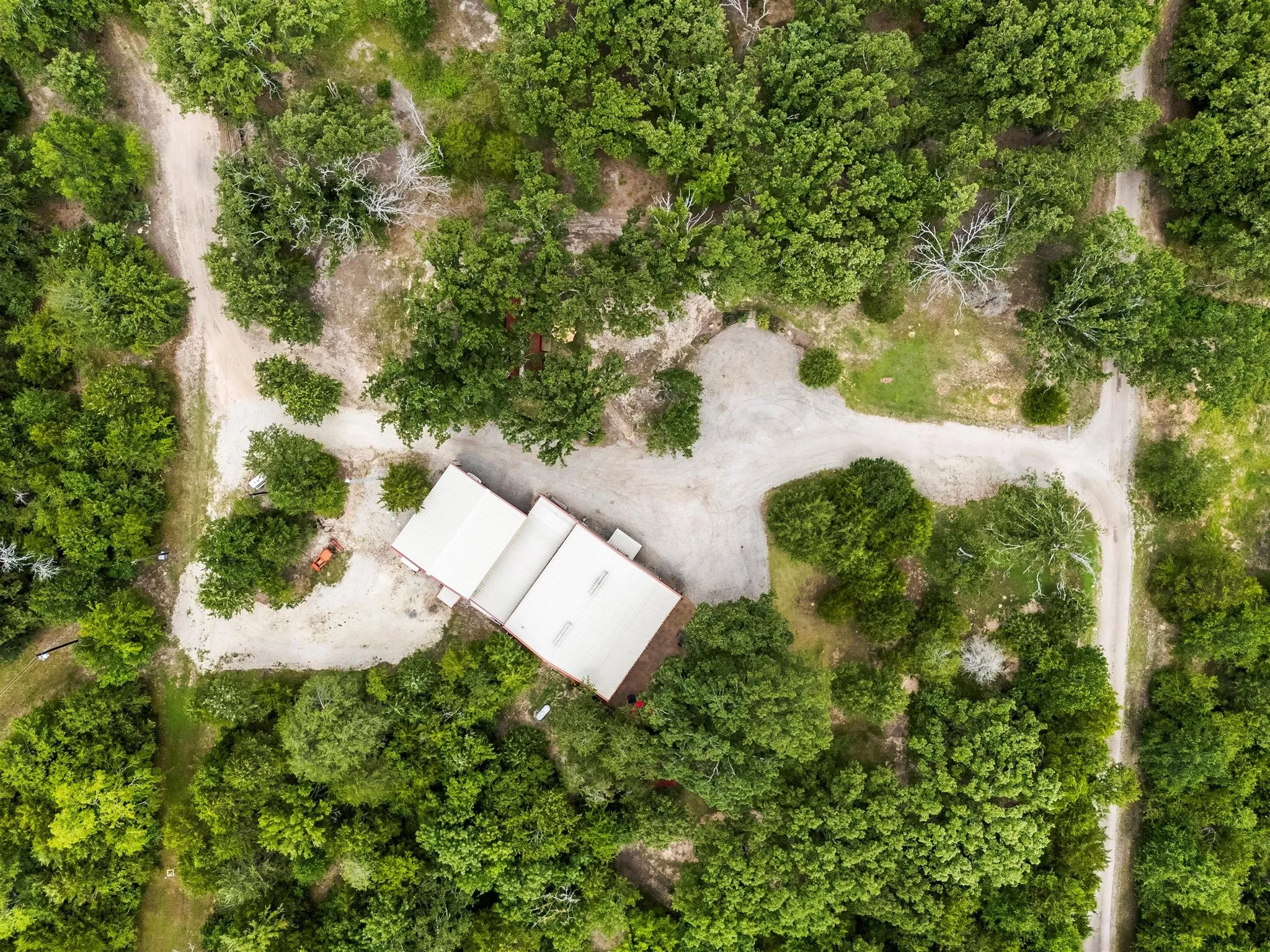 Aerial perspective showcasing a light-colored metal roof structure surrounded by extensive tree coverage