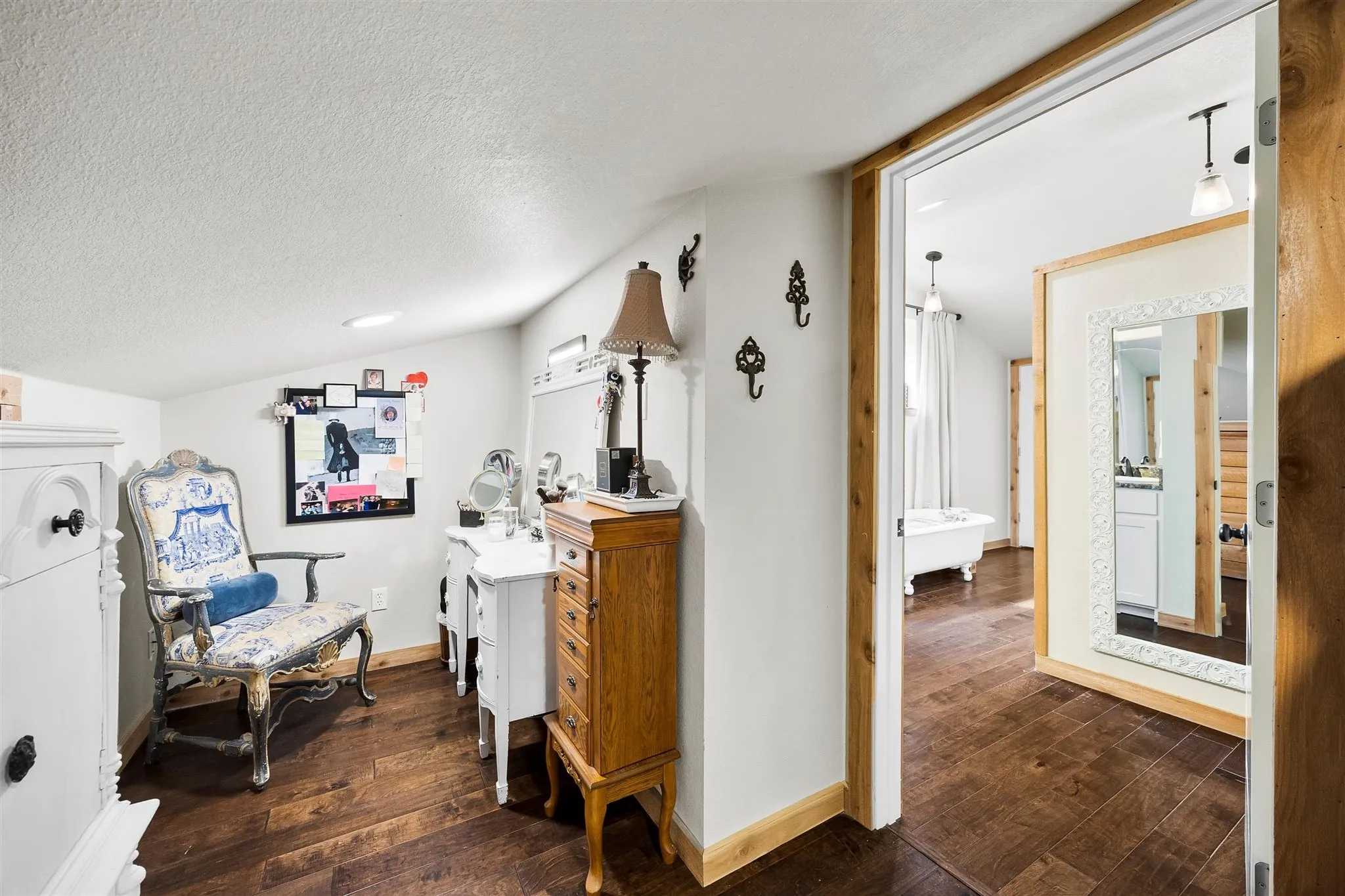 Rich wood-finish flooring extends from the dressing area into the adjacent bath, featuring a freestanding claw-foot tub and a single vanity with a white countertop