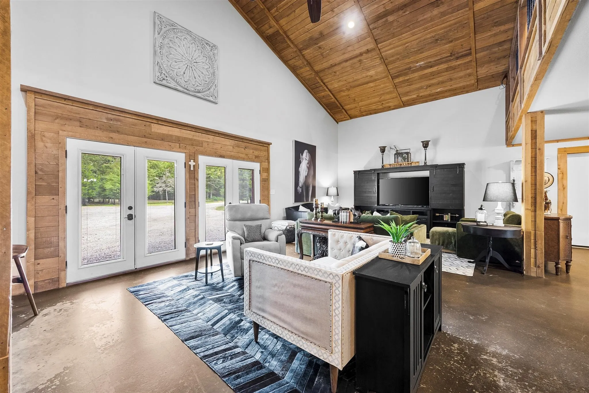Vaulted ceiling with wood-finish planks, accent wall with wood-finish paneling, polished concrete flooring, double French doors, and a built-in media console