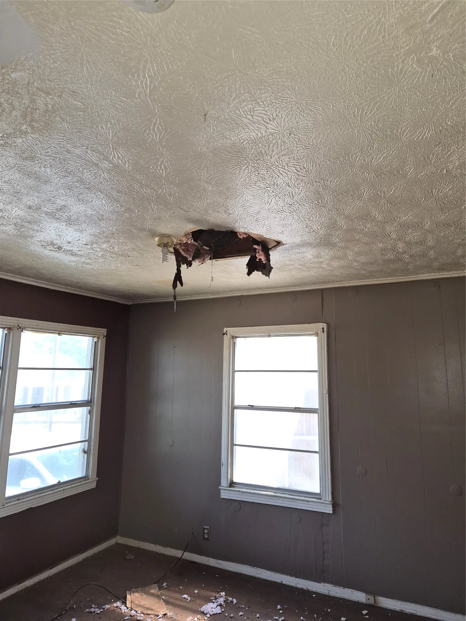 Room with textured ceiling, two windows, and dark wall paneling