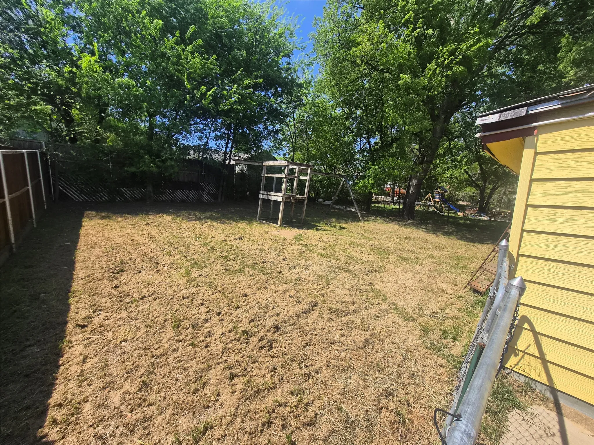 Expansive backyard featuring mature trees, a wooden privacy fence, and a chain-link fence