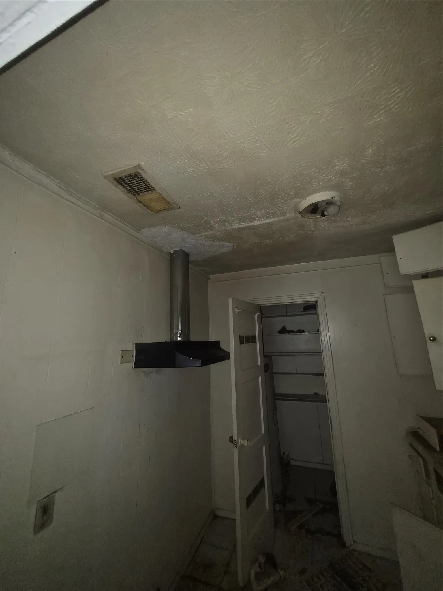 Kitchen area featuring a stainless steel range hood, overhead ceiling vent, and a pantry with shelving