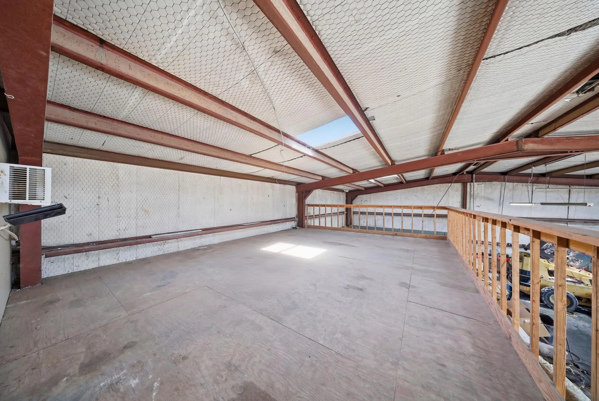 Spacious mezzanine level with wood-finish flooring, exposed metal beam ceiling structure, and a wood railing