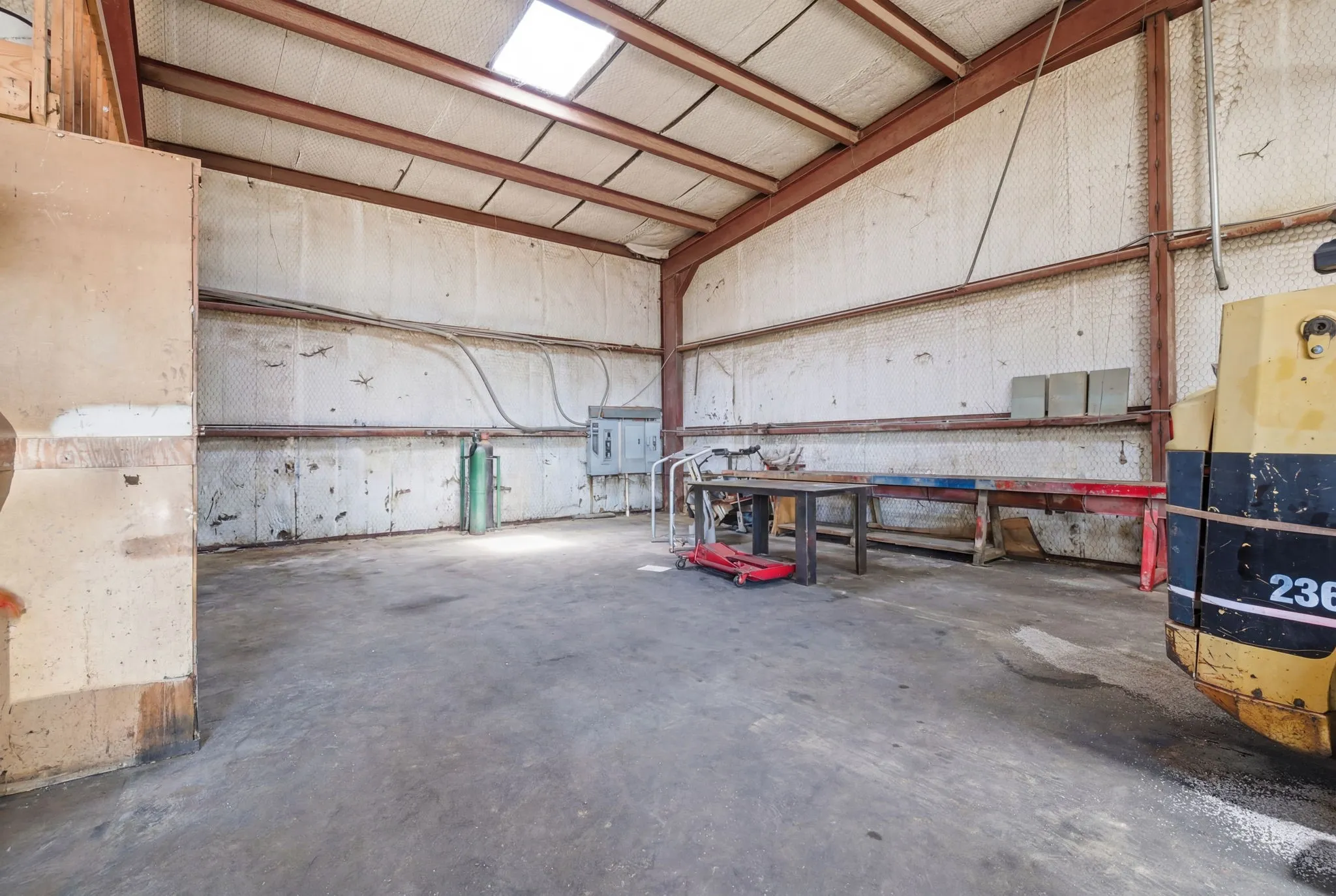 Industrial interior featuring a skylight, exposed metal beams, concrete flooring, and insulated paneling