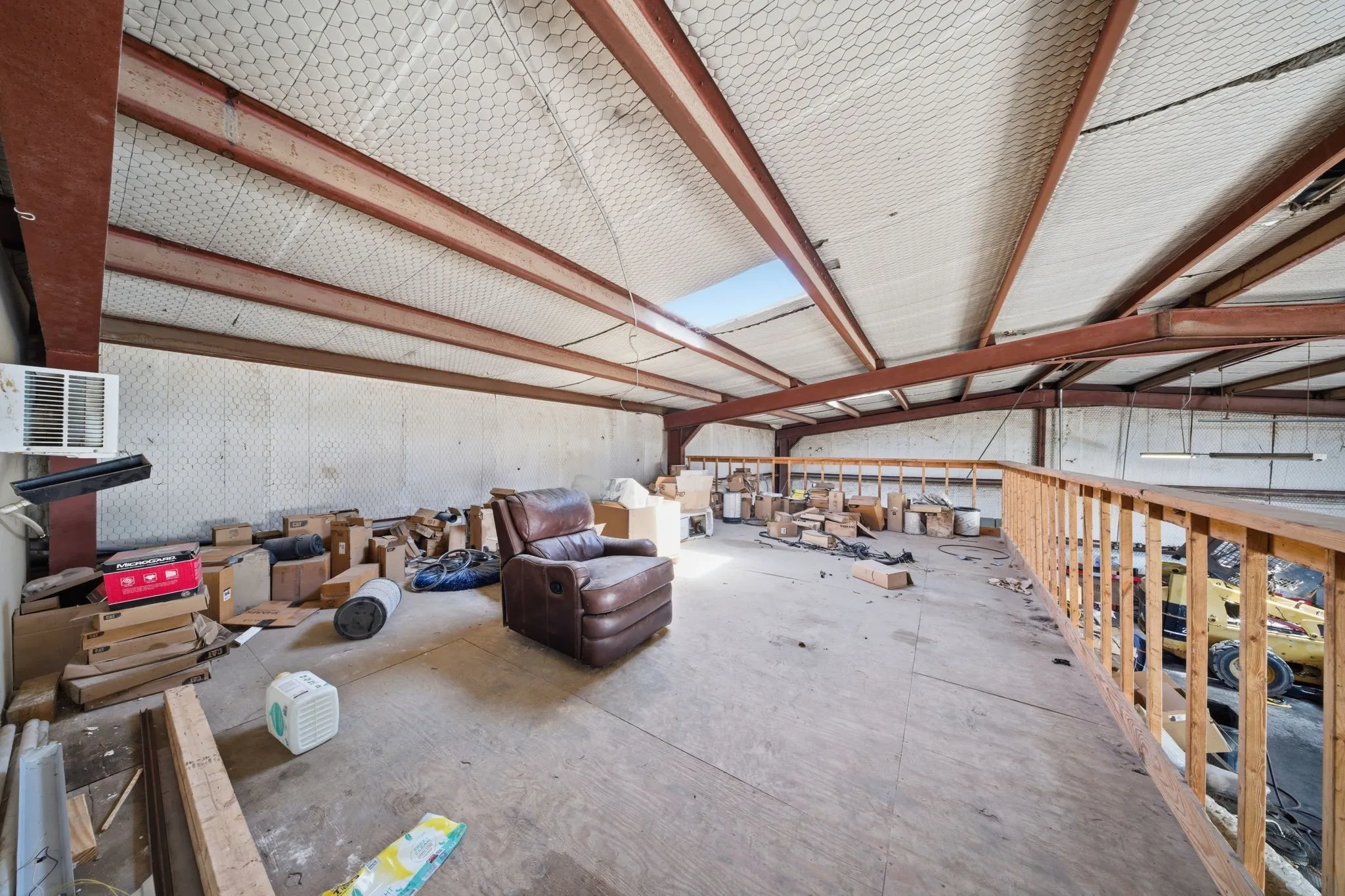 Large open-concept space featuring exposed structural beams, a skylight, and a partial wood railing
