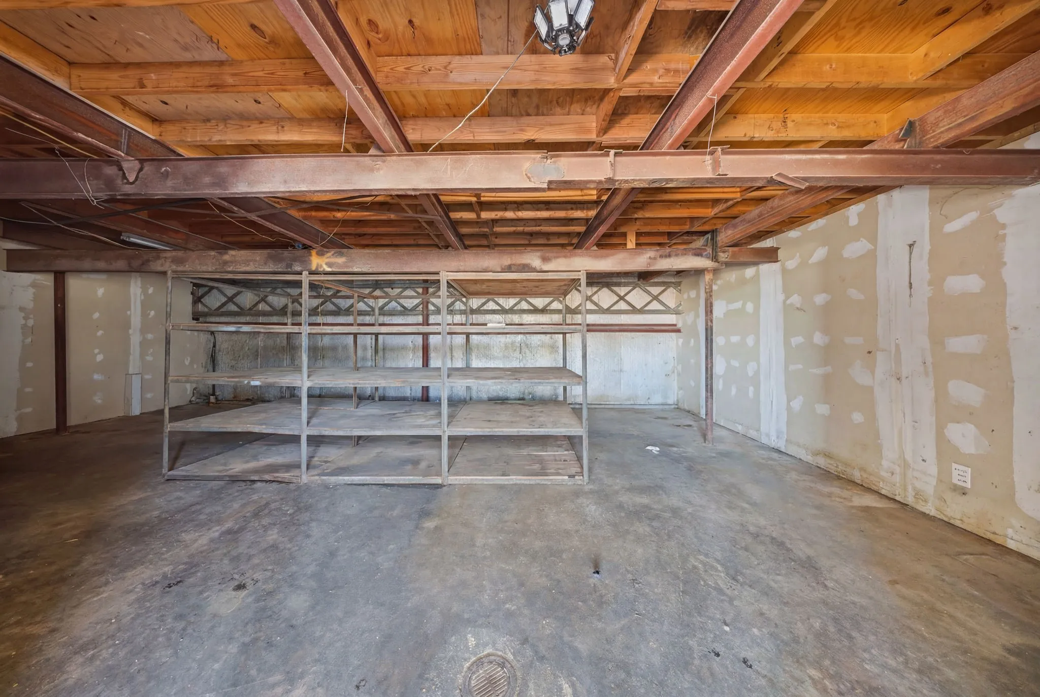 Open space with exposed wood ceiling beams, concrete flooring, and metal shelving units
