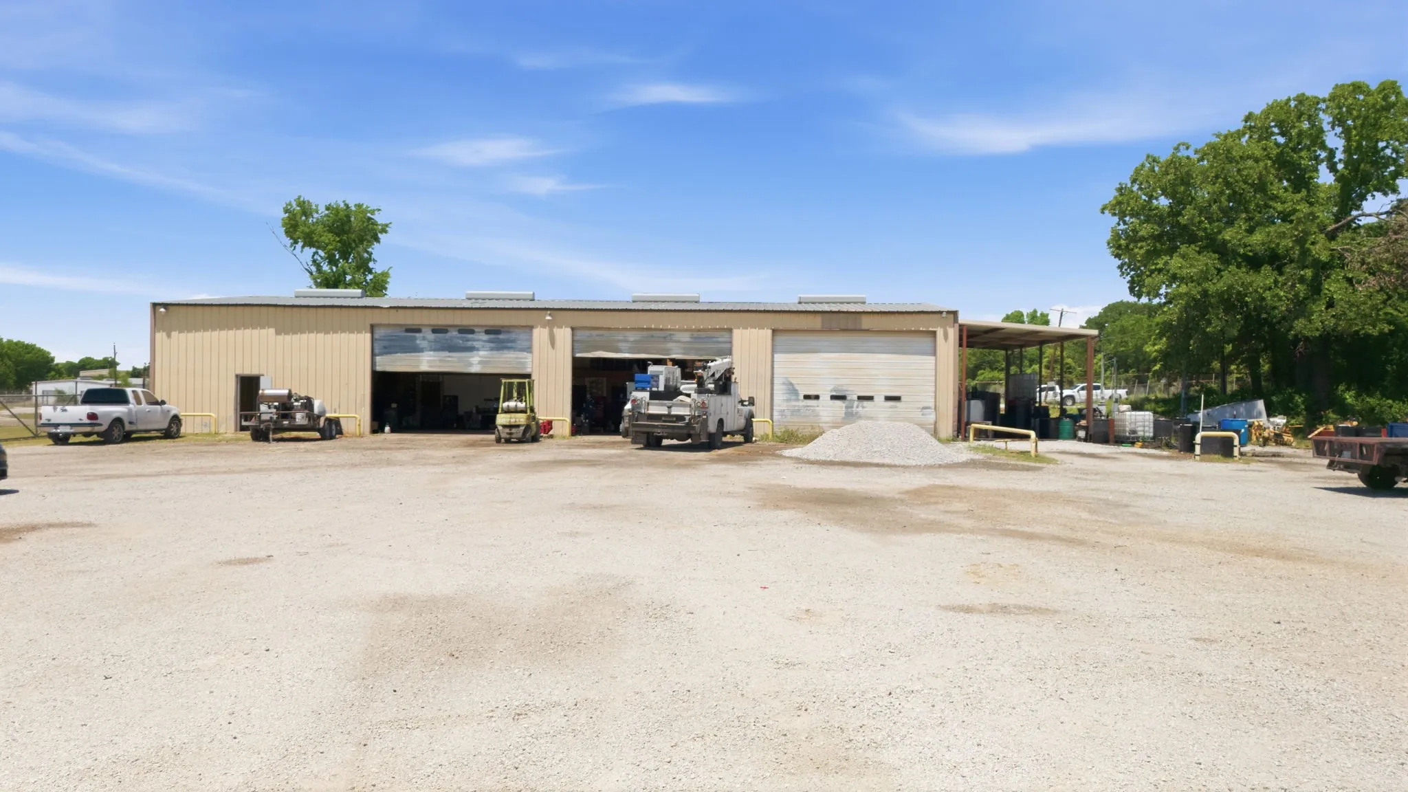 Industrial building with a tan metal exterior, multiple large roll-up doors, and an expansive gravel lot