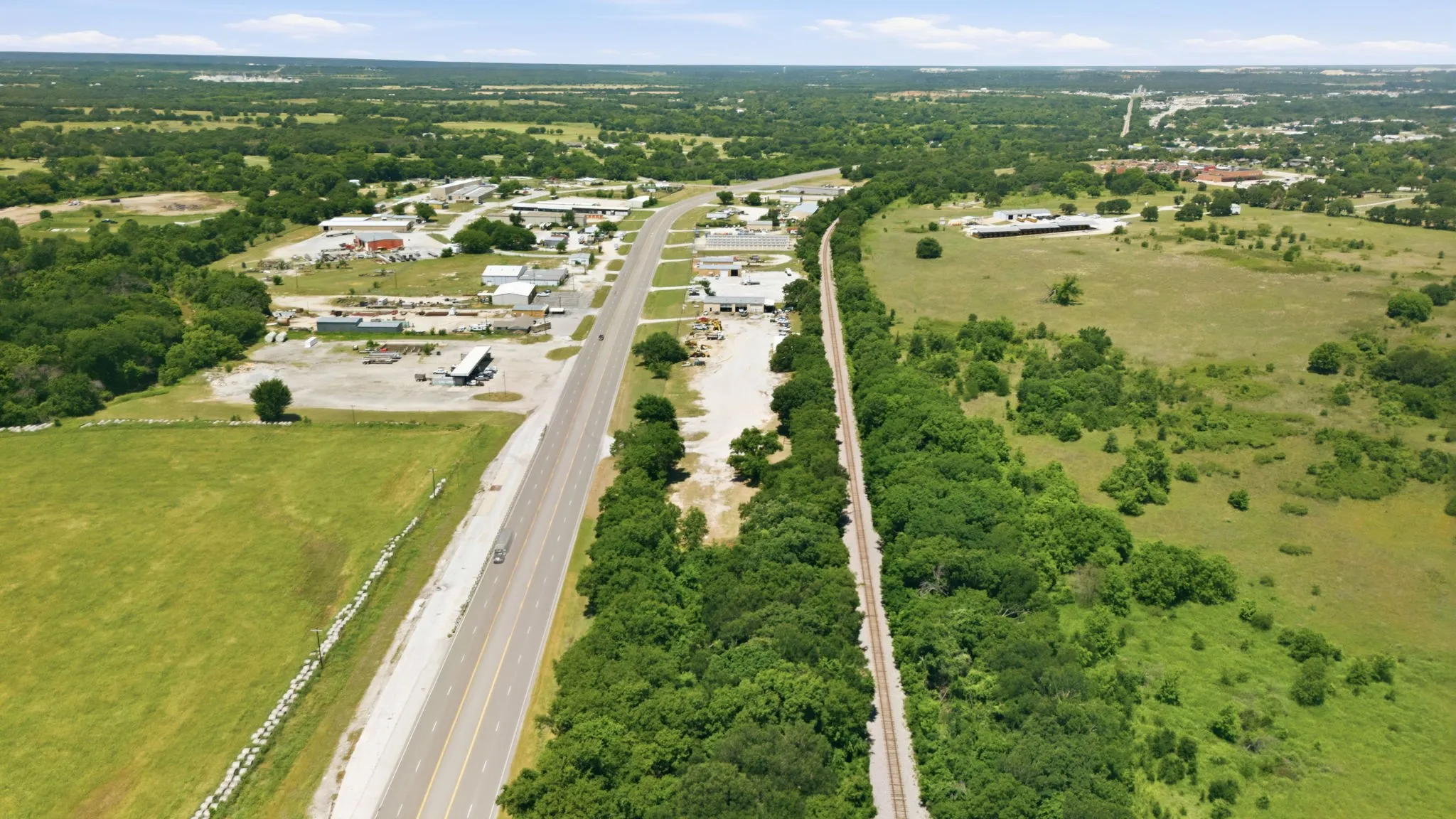 Extensive land parcel featuring a multi-lane paved road, an active railway line, and abundant green foliage