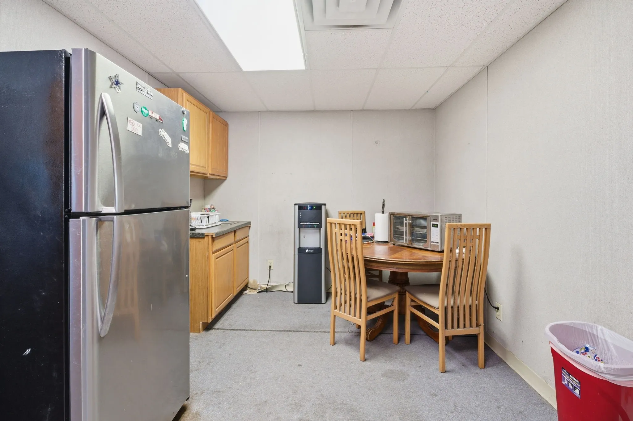Functional kitchen space featuring light wood cabinetry, a stainless steel refrigerator, and a round wood-finish dining table with matching chairs
