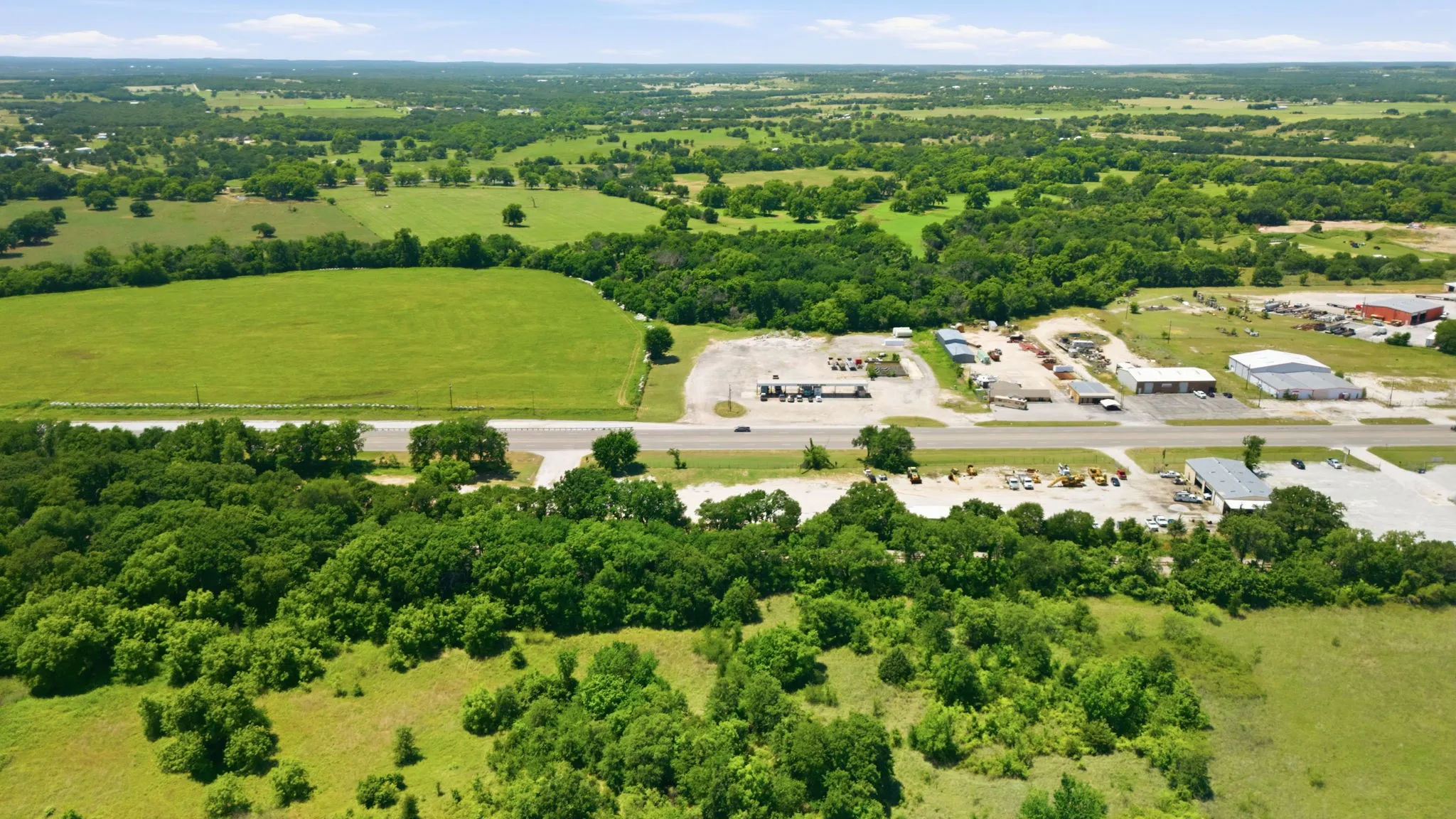 Expansive green landscape featuring a prominent roadway, surrounding fields, and established tree lines