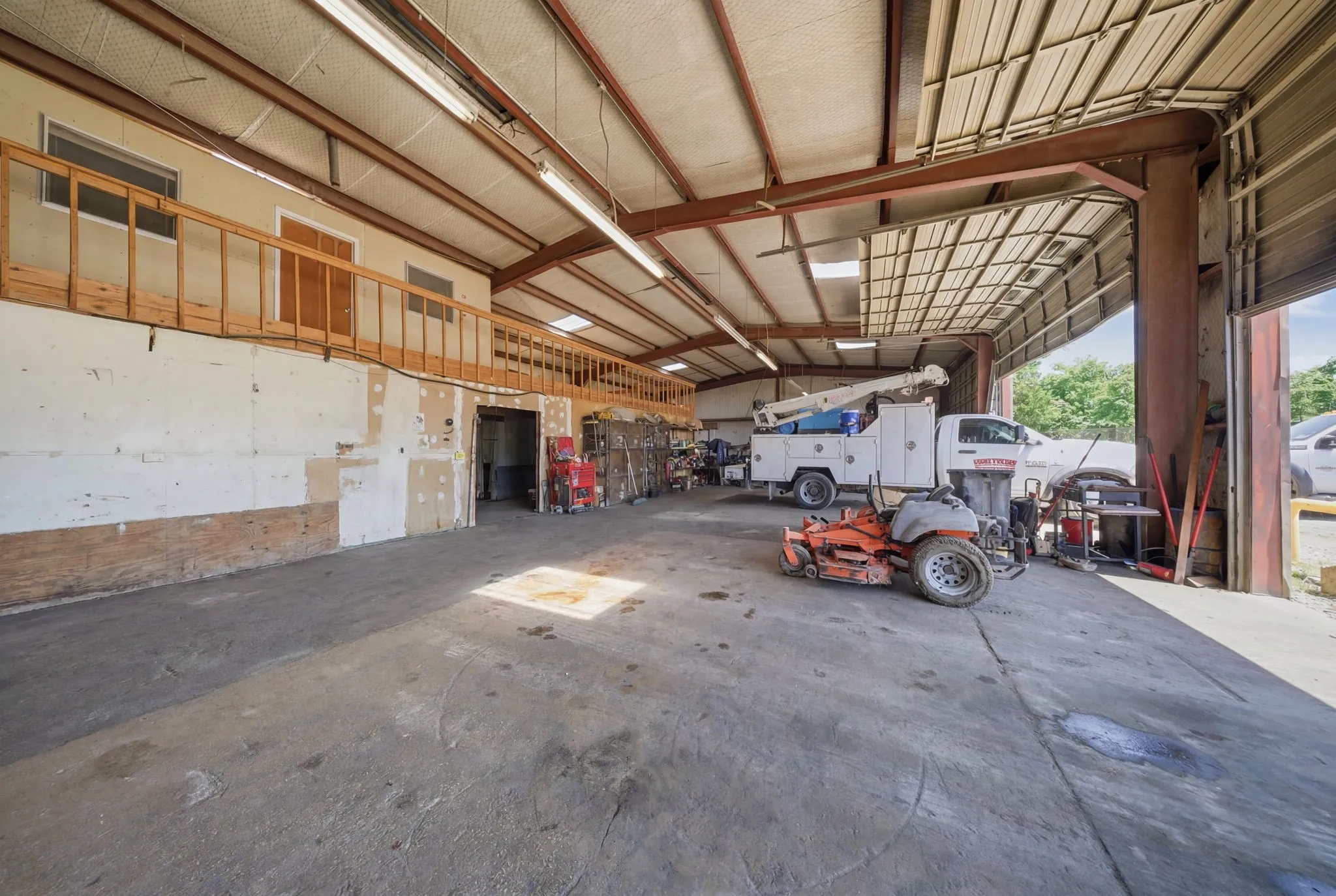 Spacious industrial-style interior featuring a concrete floor, high ceilings with exposed metal beams, and fluorescent lighting