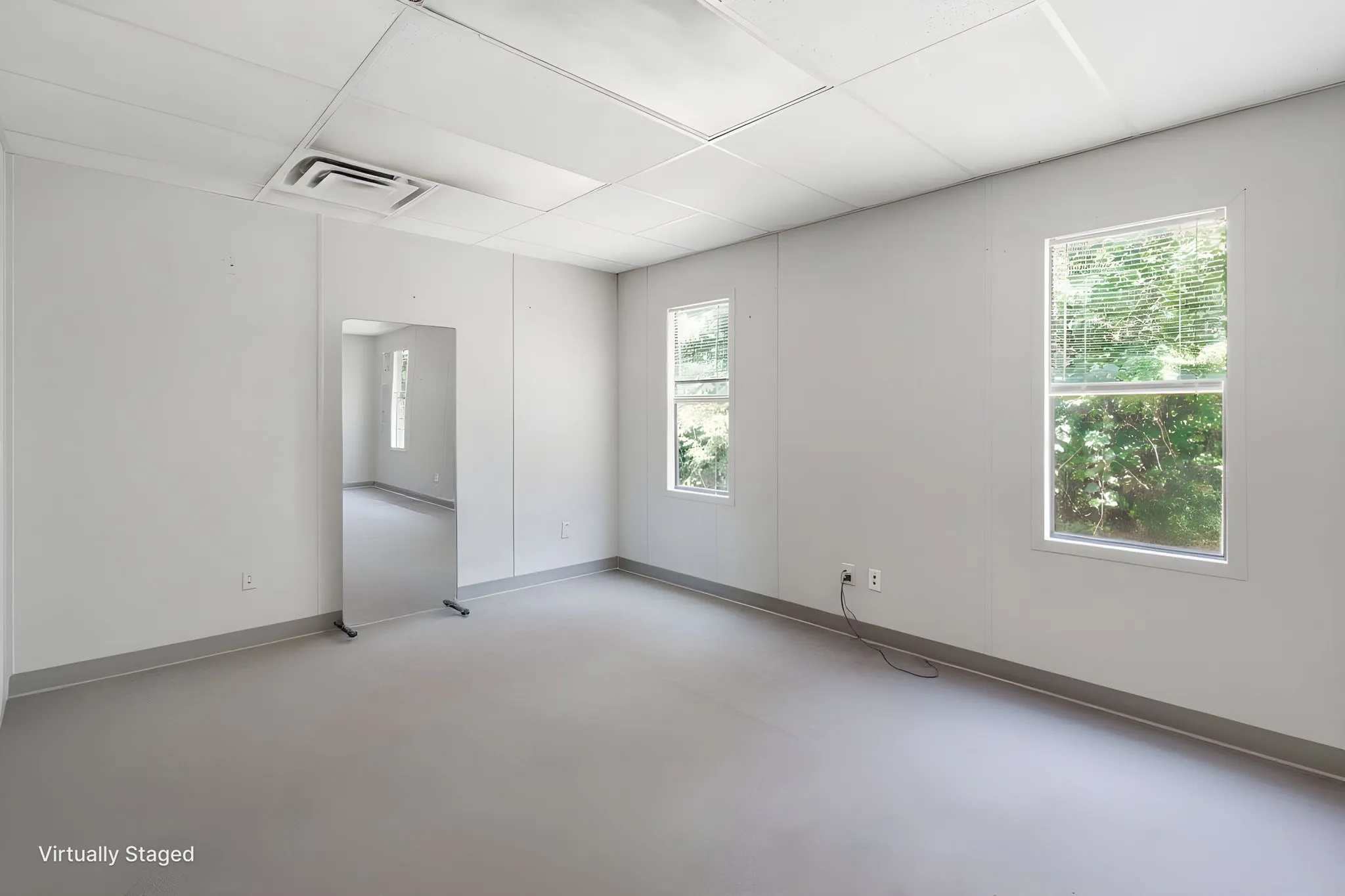 Spacious room featuring light gray walls, large windows, acoustic tile ceiling, and neutral flooring