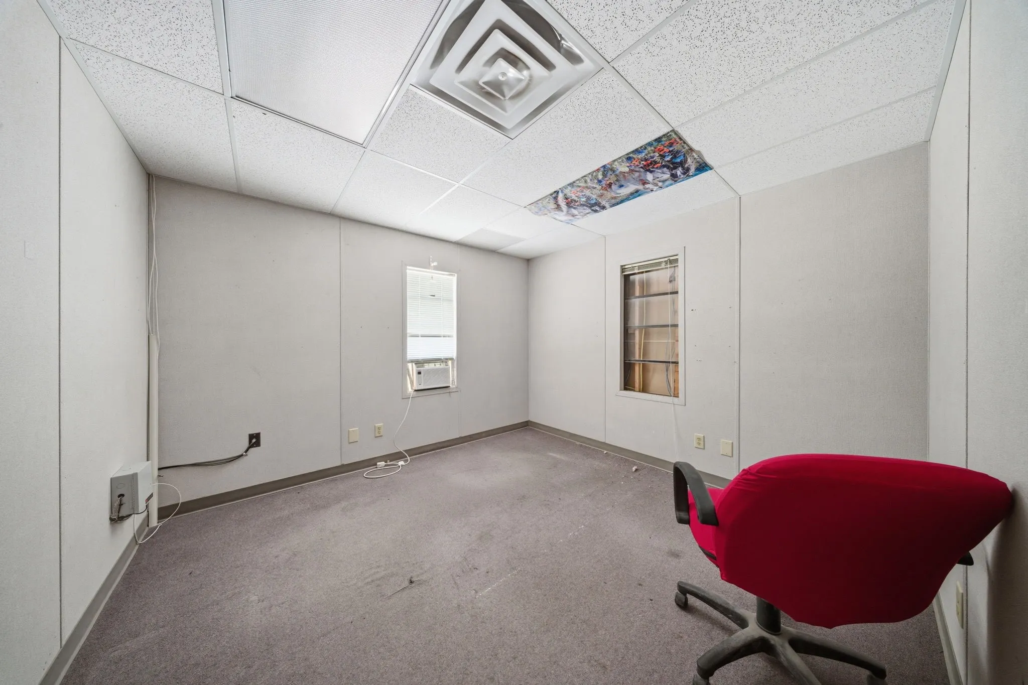 Room featuring two windows, drop ceiling with integrated lighting, and wall-mounted electrical outlets