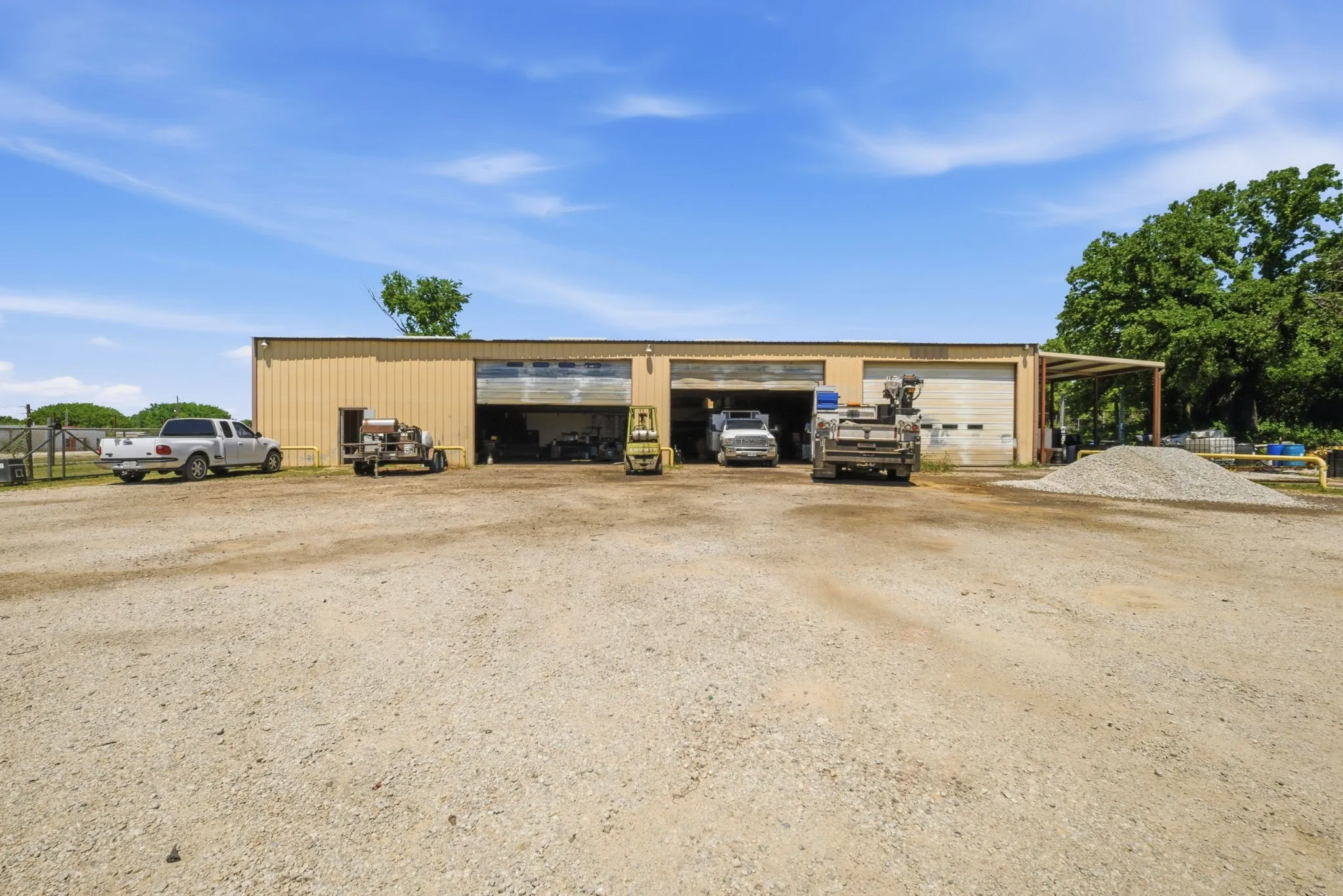 Industrial building featuring a metal facade, multiple bay doors, and an expansive gravel lot