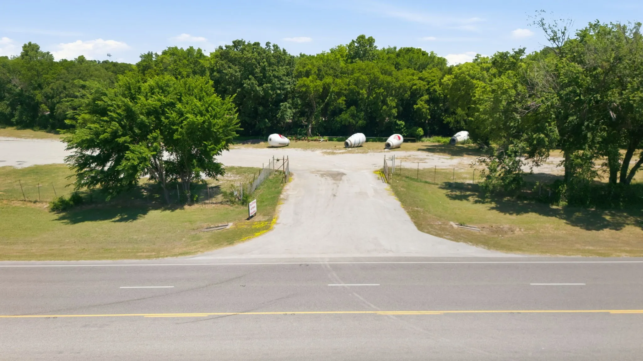 Paved road frontage with a gravel drive entrance and fenced perimeter