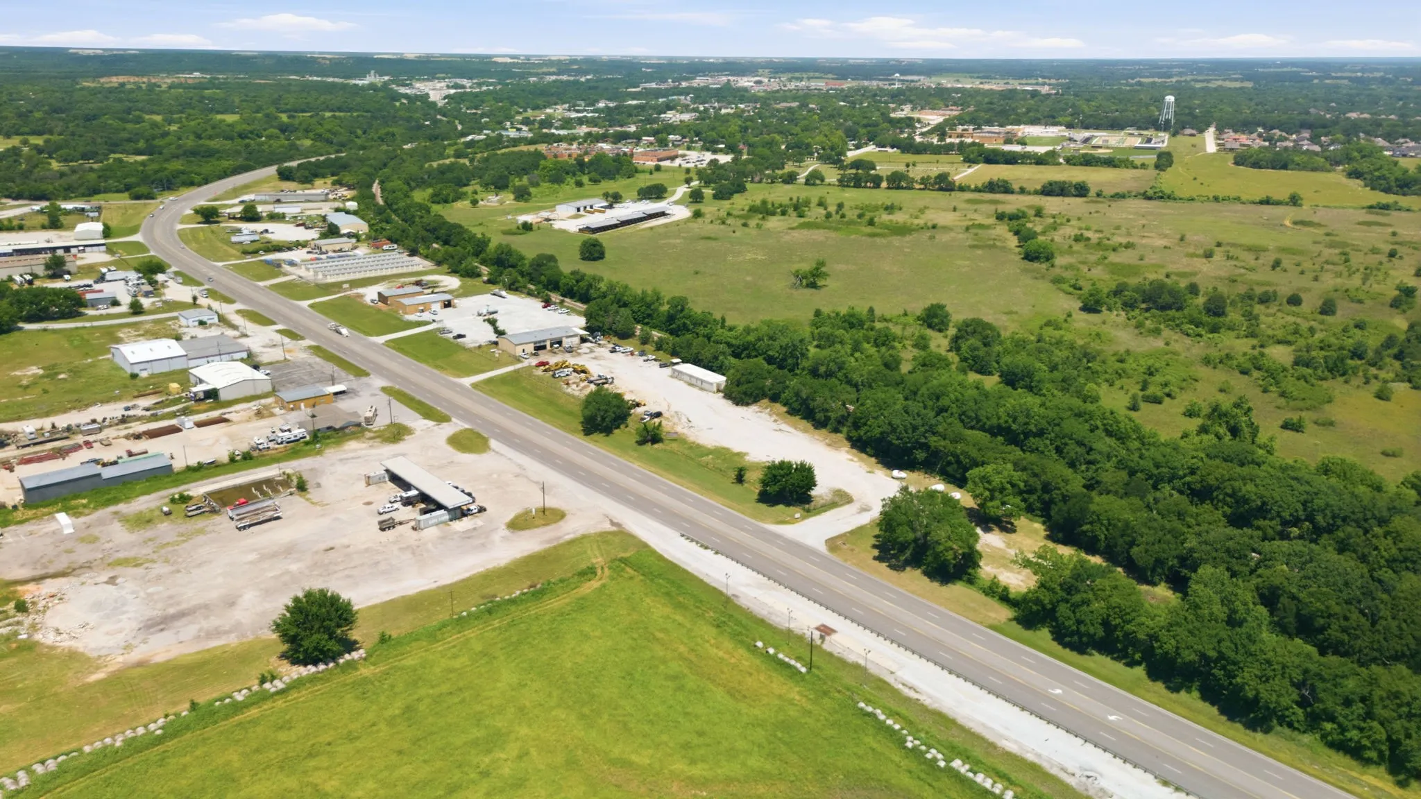 Expansive land parcel featuring direct road frontage, multiple existing structures, a substantial treeline, and surrounding green space
