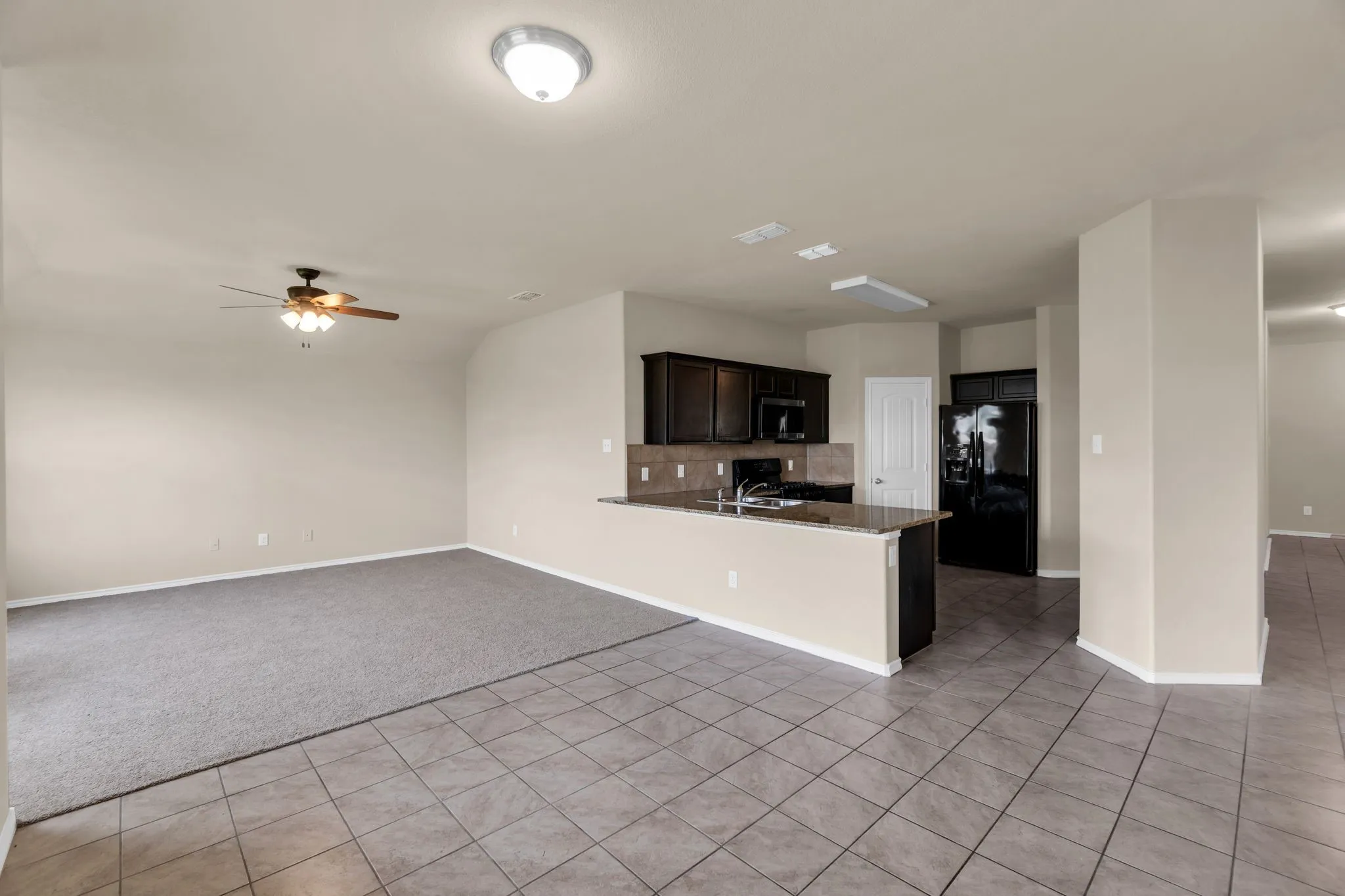 Kitchen with ceiling fan, kitchen peninsula, light colored carpet, backsplash, and black fridge with ice dispenser