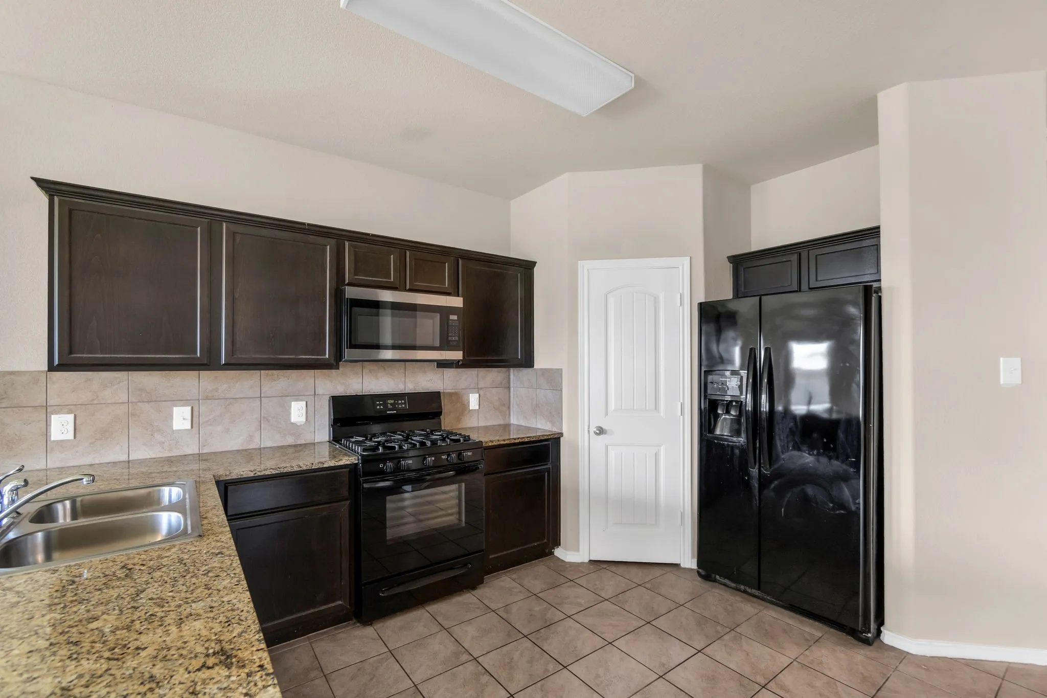 Kitchen with black appliances, sink, tasteful backsplash, and light tile flooring