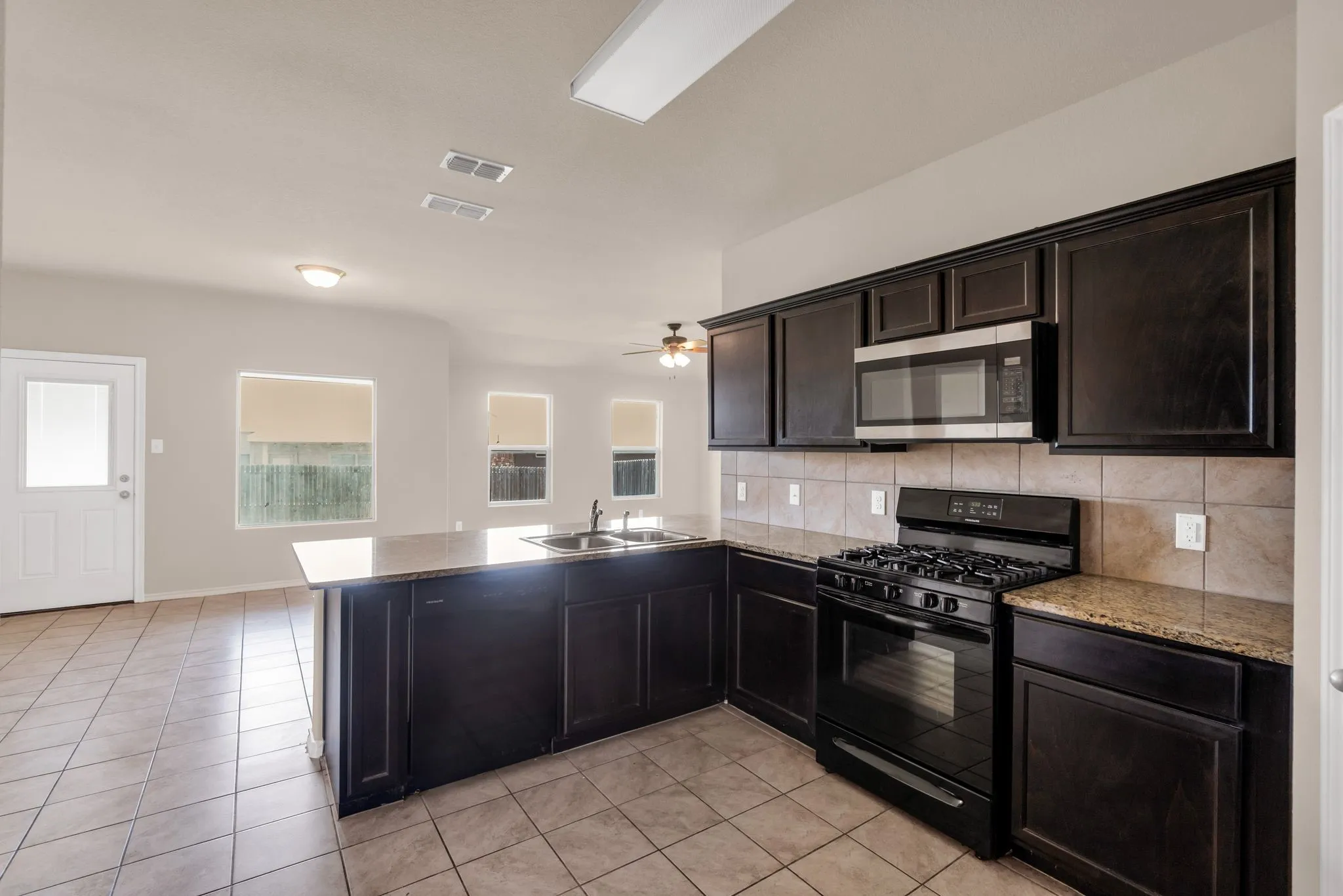 Kitchen featuring gas stove, kitchen peninsula, light stone counters, sink, and light tile floors