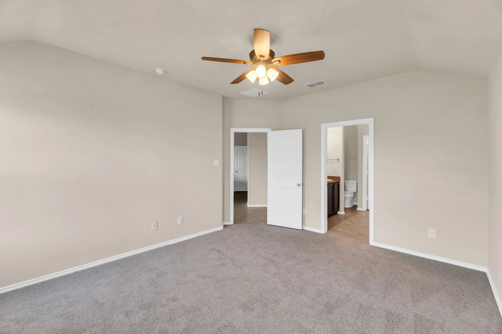 Unfurnished bedroom featuring carpet, ensuite bathroom, vaulted ceiling, and ceiling fan