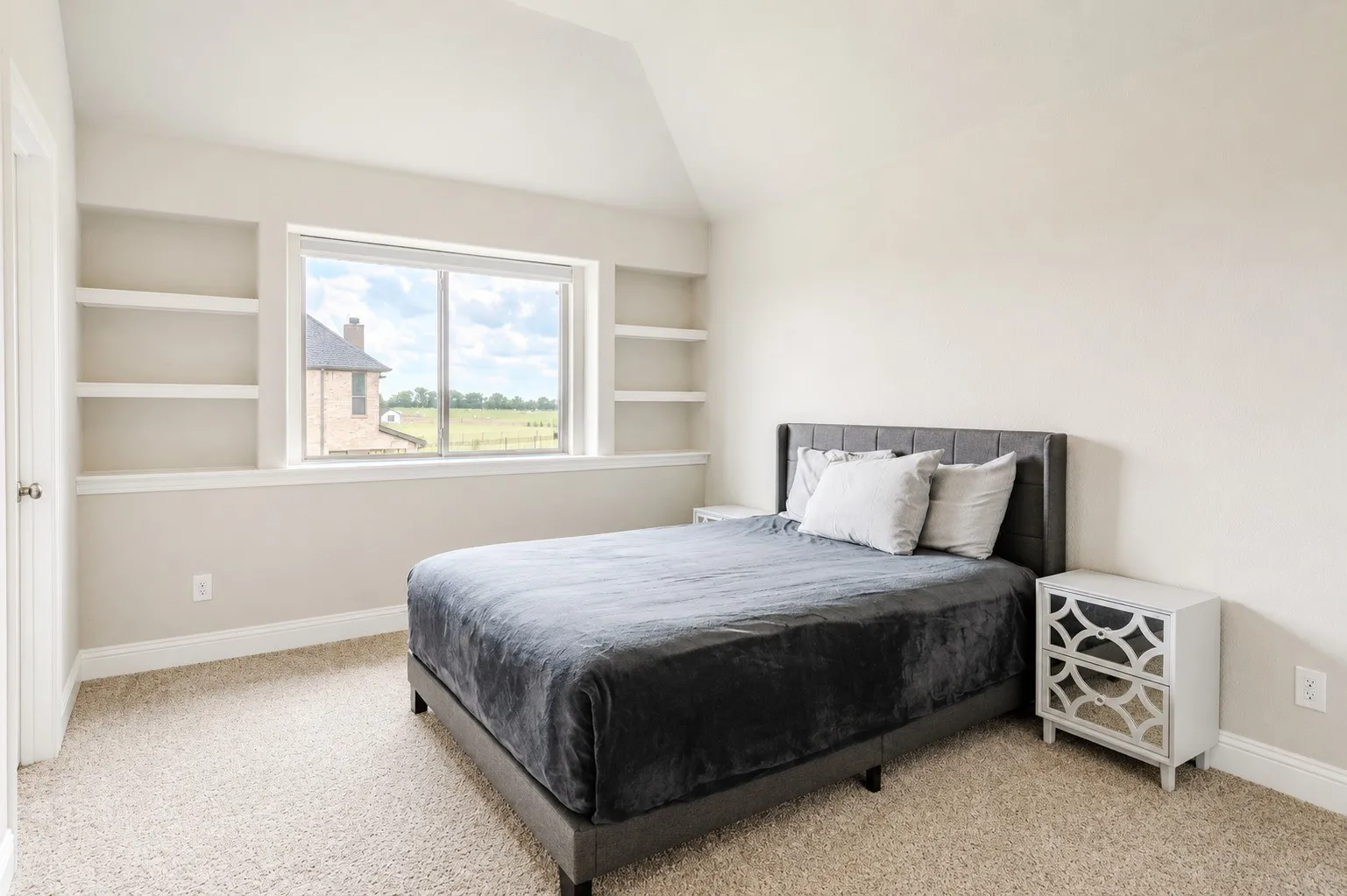 Carpeted bedroom featuring a large window with built-in shelving, vaulted ceiling, and baseboard trim