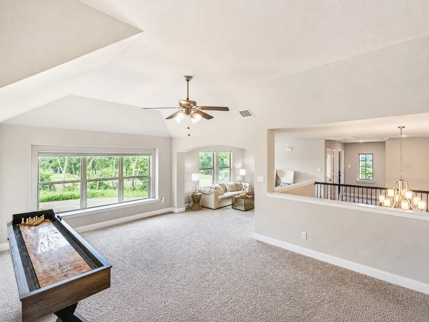 Spacious second-level living area featuring vaulted ceilings, a ceiling fan with integrated lighting, multiple windows, and plush carpeting