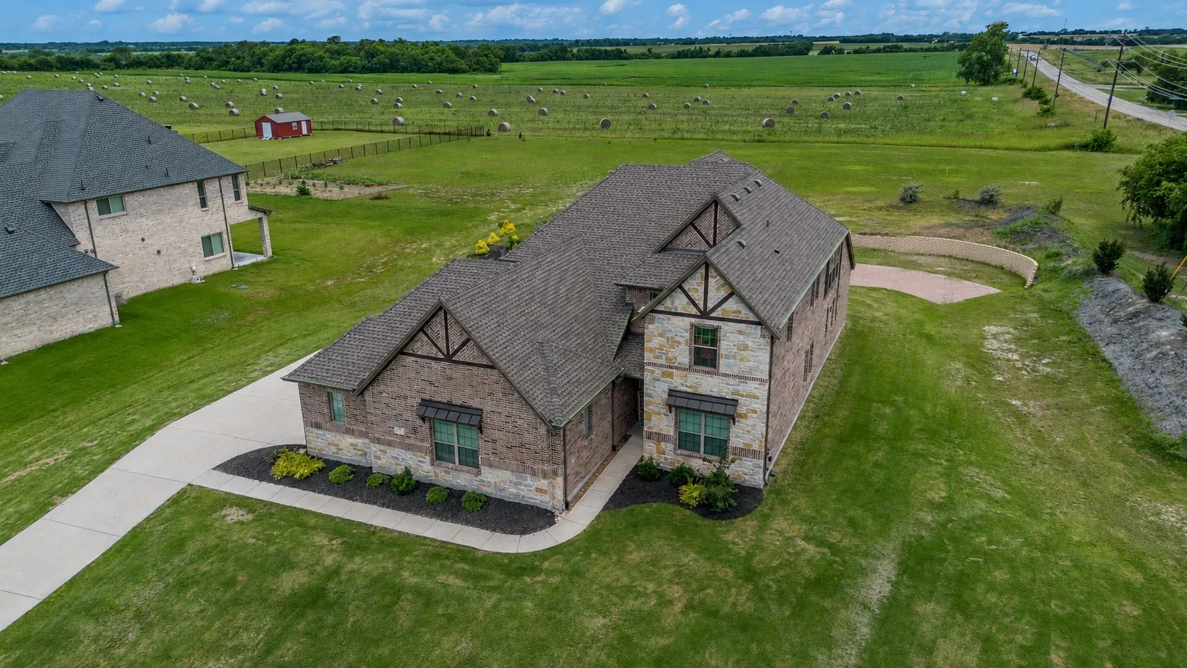 Exterior featuring stone and brick facade, a multi-gabled roofline, decorative timber detailing, front landscaping, and an extended concrete driveway