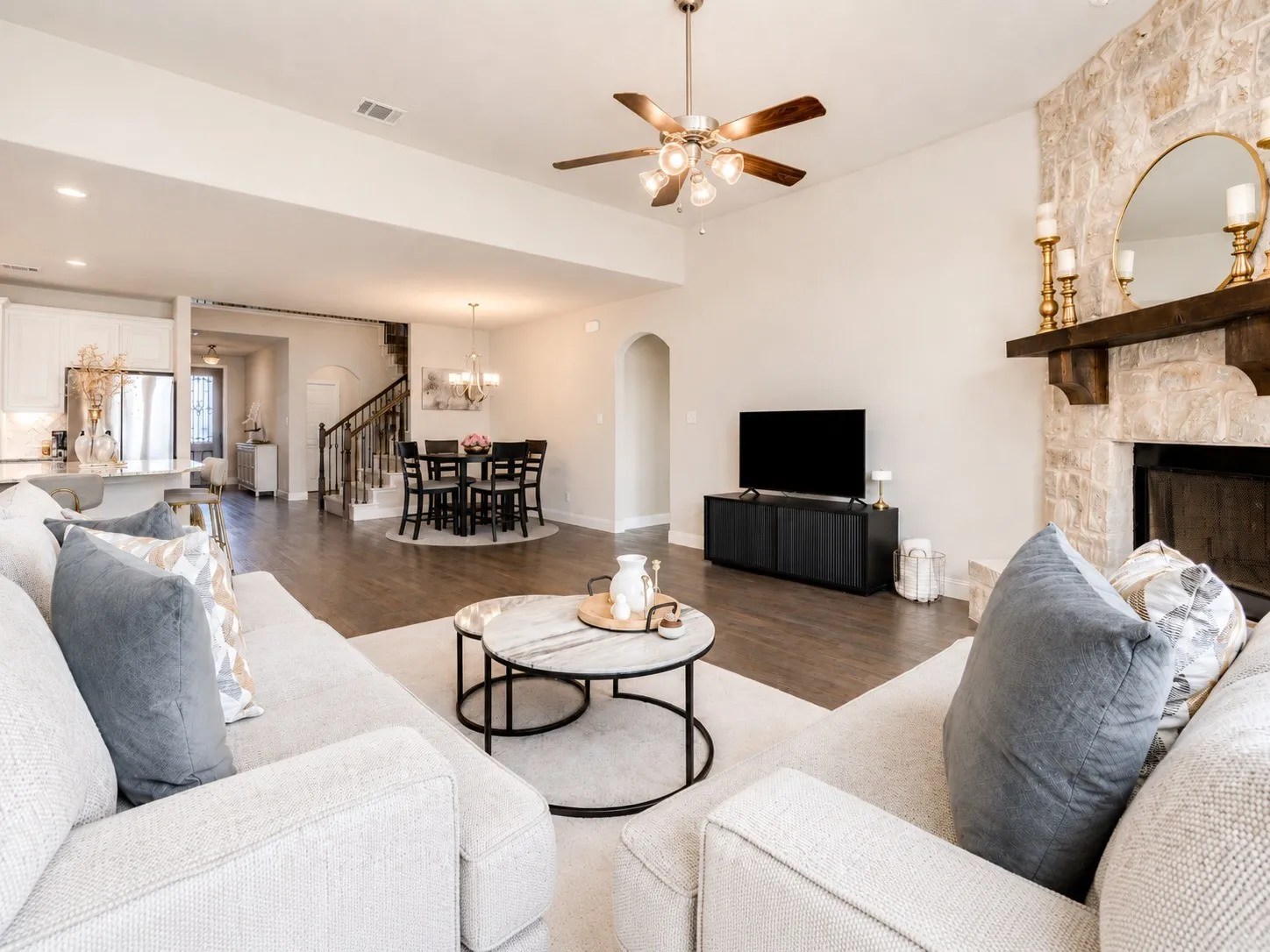 Spacious interior featuring a stone fireplace with a wood-beam mantel, wood-finish flooring, and a ceiling fan with integrated lighting