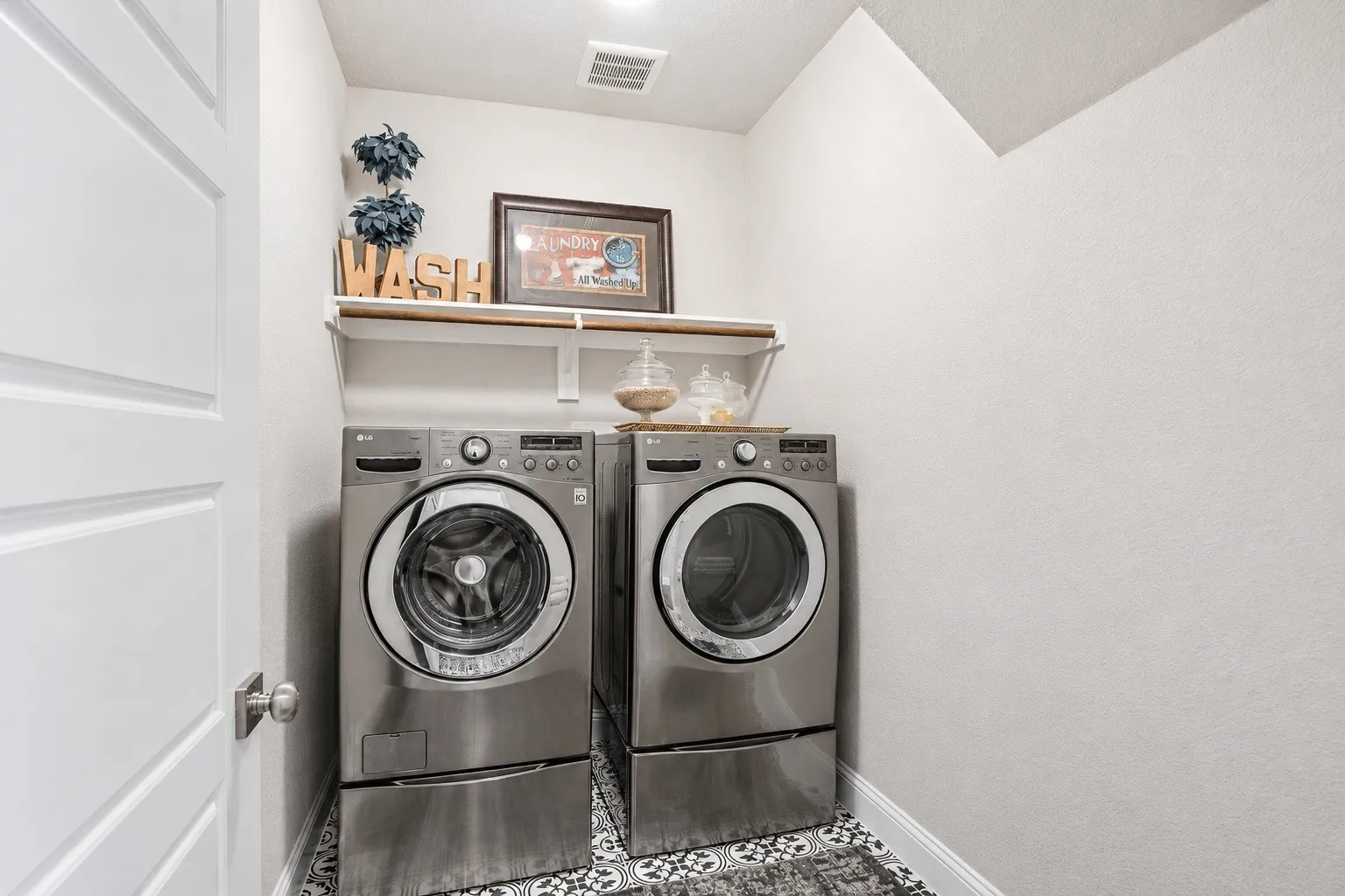 Dedicated laundry area featuring a patterned floor tile, overhead shelving, and a bright white door